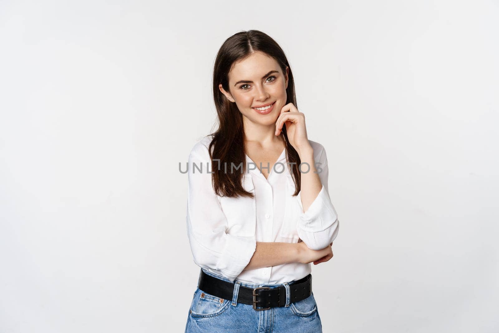 Smiling young businesswoman, female entrepreneur in white shirt, cross arms on chest like professional, standing over studio background.