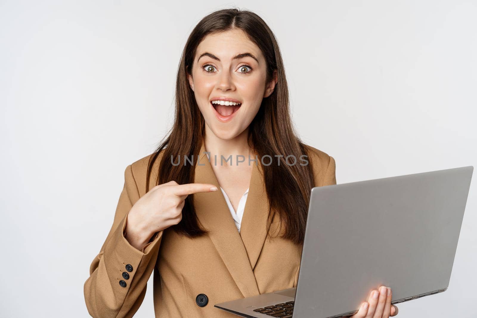 Happy businesswoman pointing at laptop screen, showing work progress and smiling excited, standing over white background. Copy space