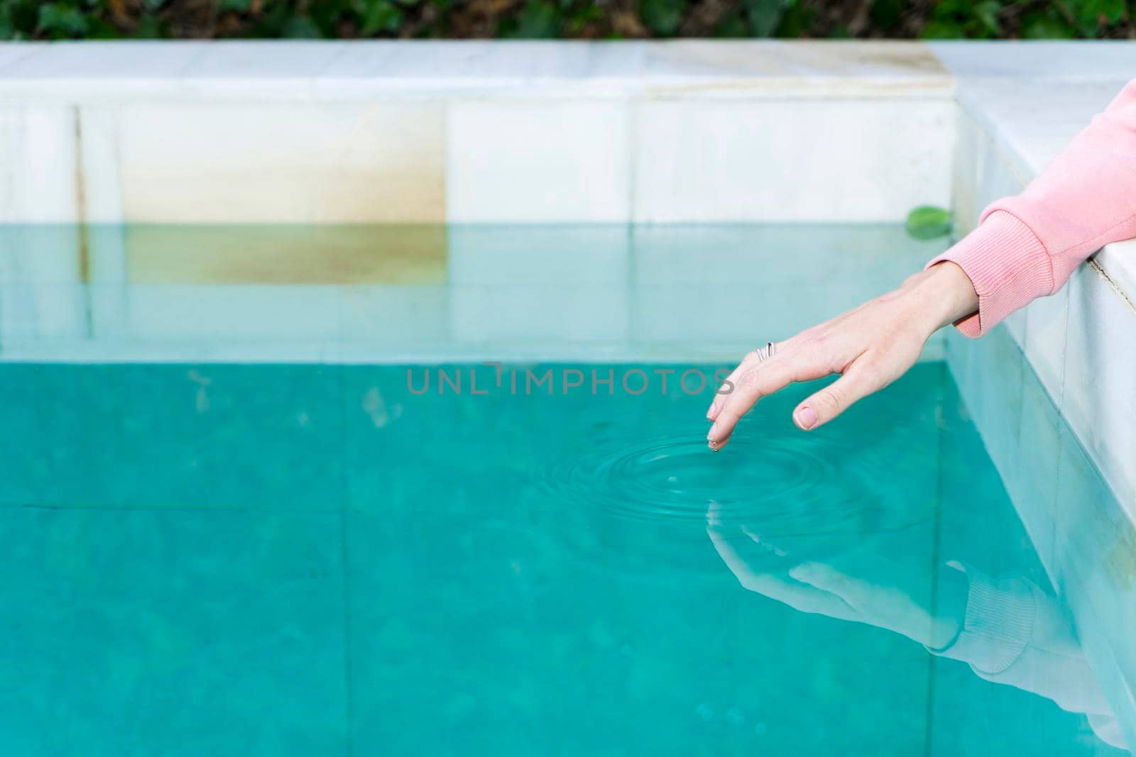 Young woman's hand delicately touching the surface of a turquoise-blue pool and generating a small ripple.