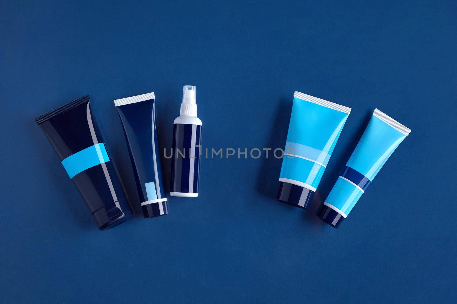 Four colorful different sized tubes and pump bottle with no logo against blue background. Cosmetic packaging, containers. Advertising, branding area. Close up, copy space. Top view, mock up