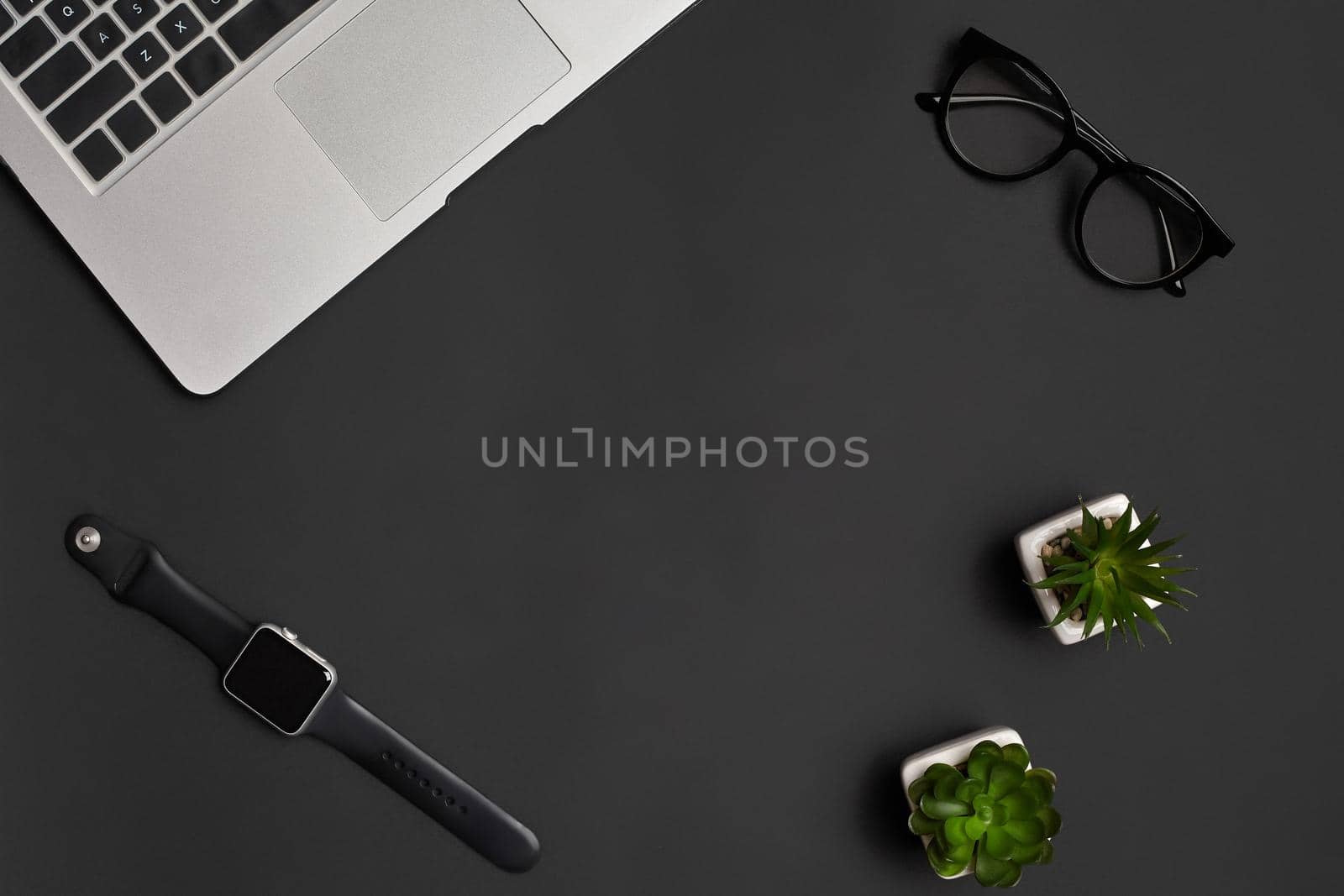 Metallic notebook or laptop, glasses, smartwatch and two green succulents in white pots on black studio background. Modern technology. Close up, copy space. Top view, flat lay, mock up