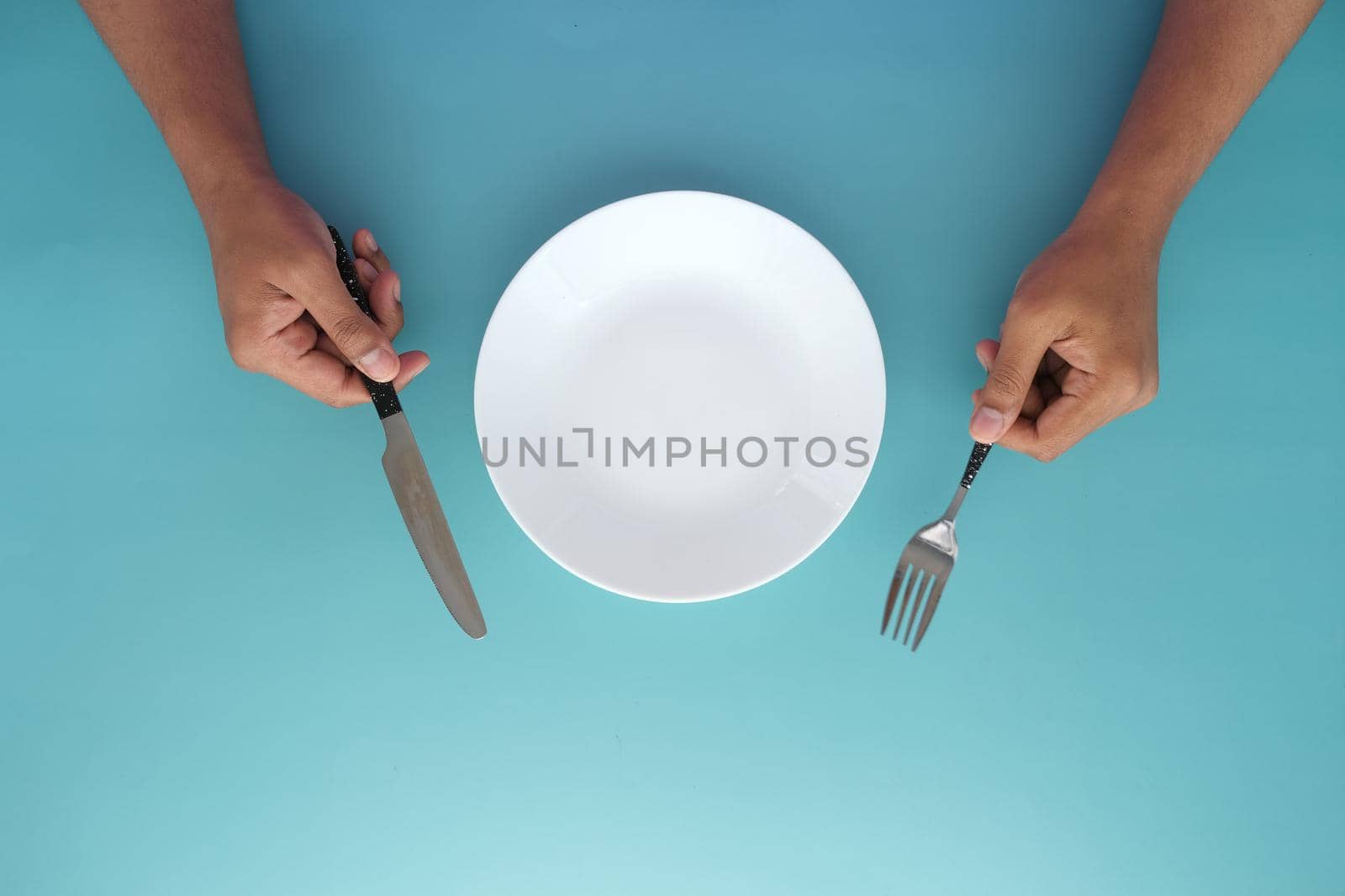 hand holding cutlery with empty plate on wooden table .