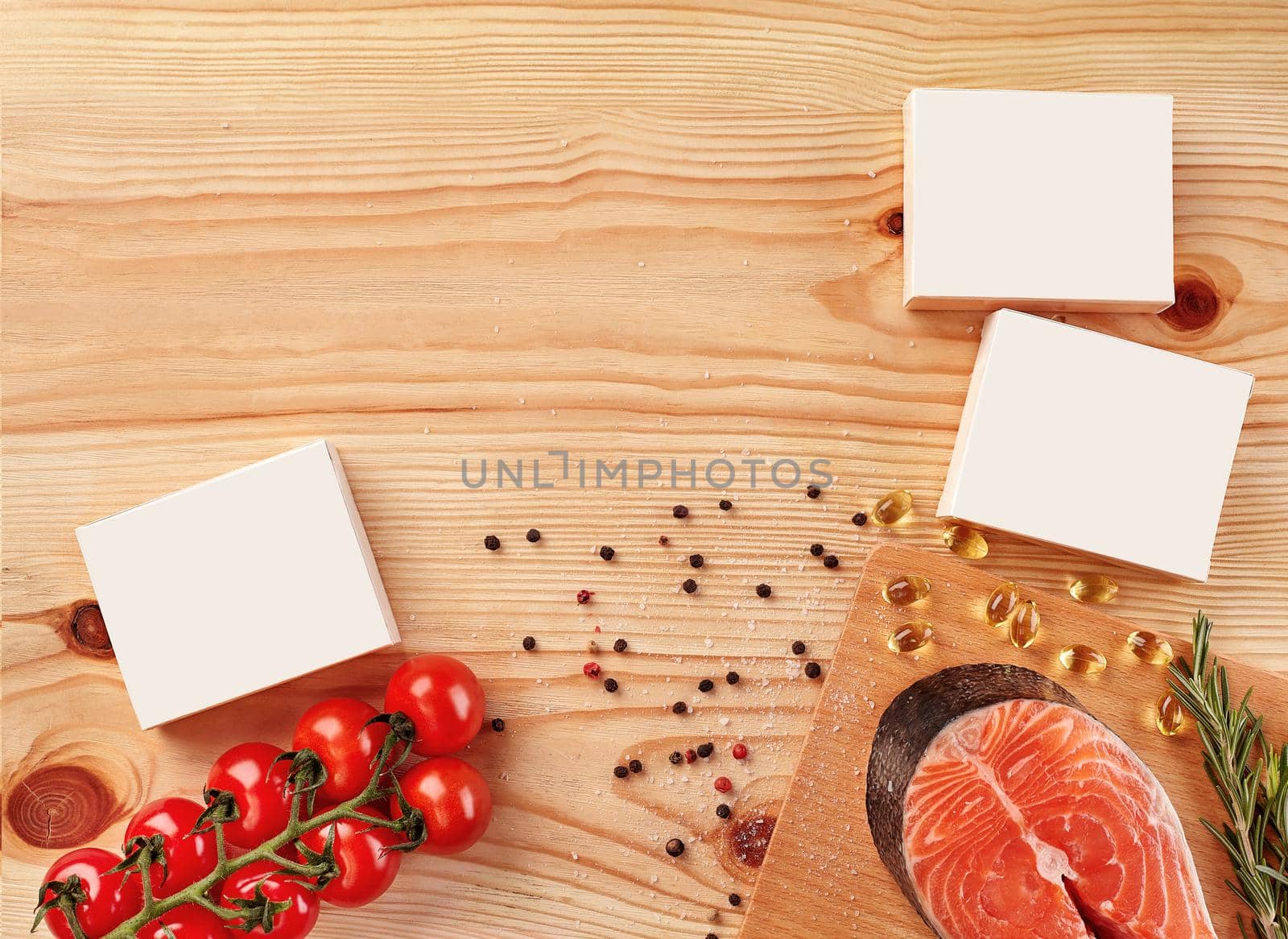 Salmon steak, twig of rosemary, cherry tomatoes, capsules, white cardboard boxes with no logo, black and red peppercorns, salt on wooden background. Close up, copy space. Mock up, top view