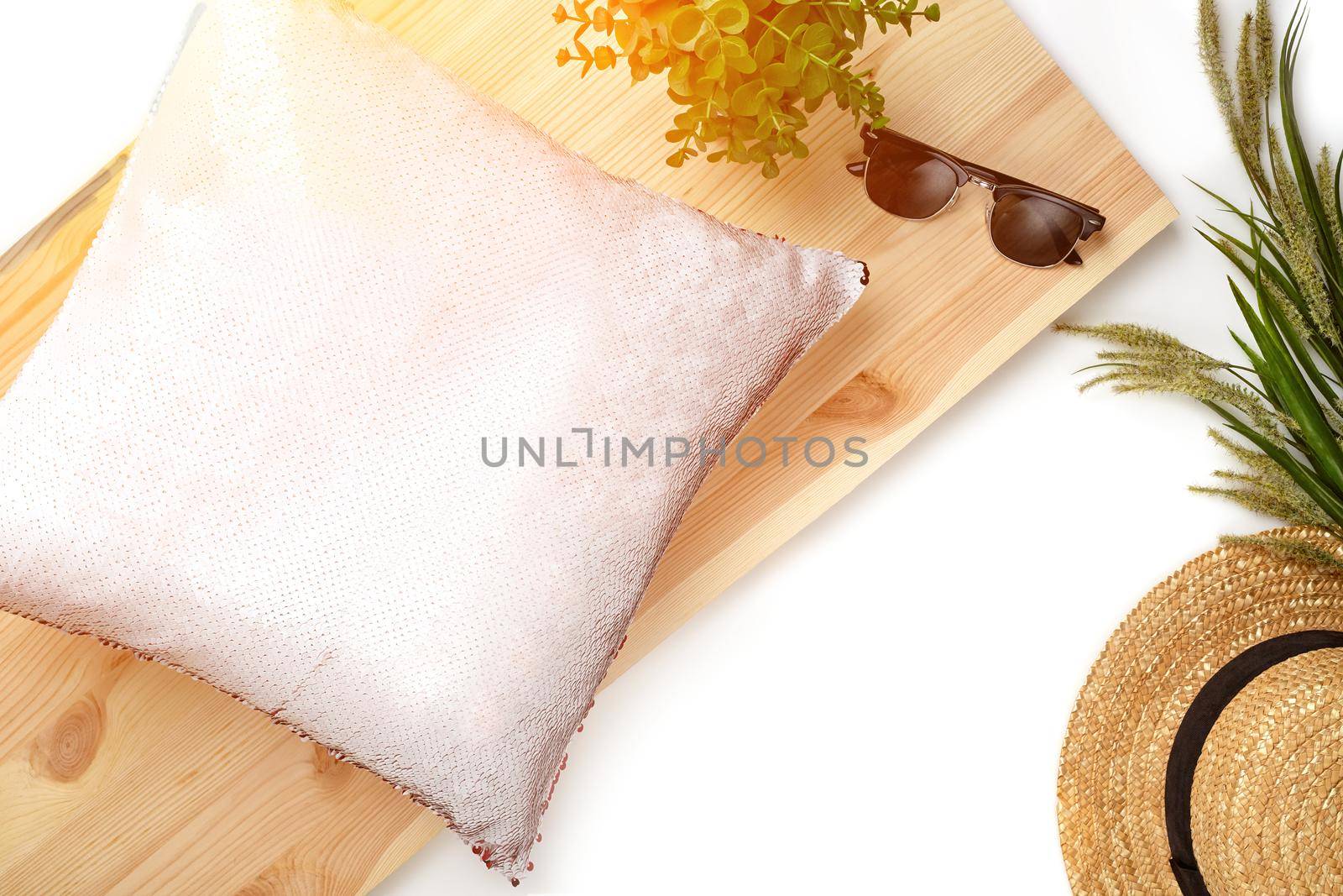 Pink pillow with sequins on wooden board next to black sunglasses, green plants and straw hat isolated on white background. Close up, copy space for your text or images. Top view, flat lay, mock up