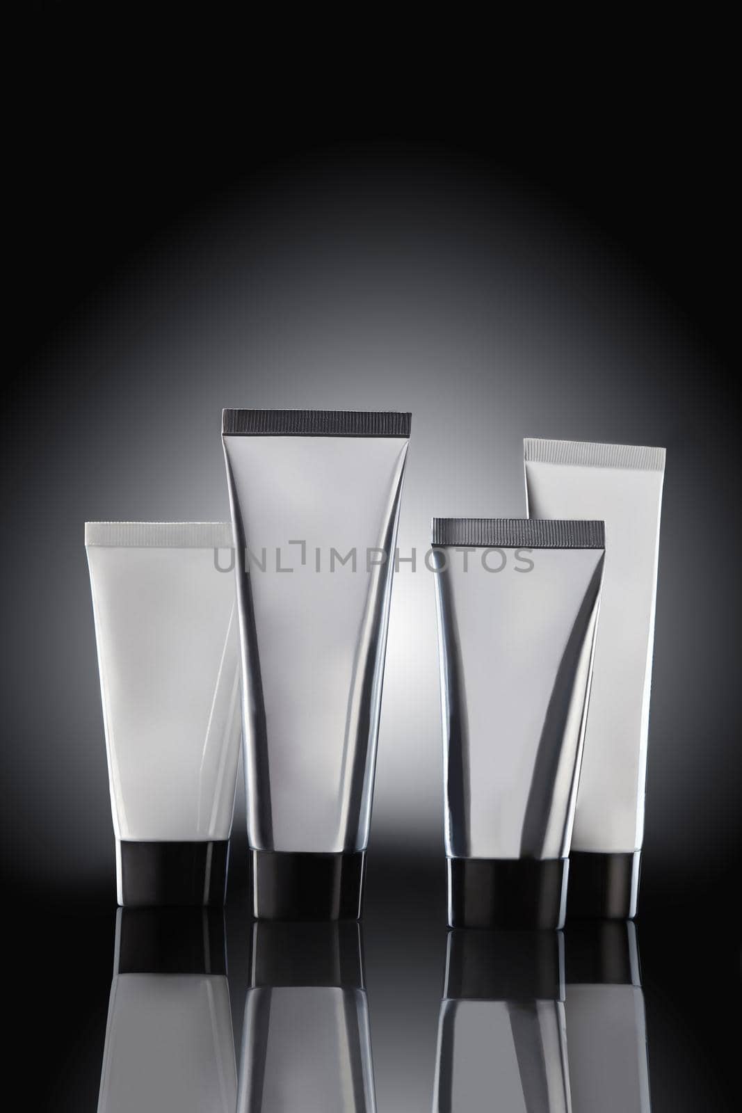 Four colorful different sized no logo cosmetic tubes on mirror surface against black background with backlight. Packaging, containers. Advertising, branding area. Close up, copy space, mock up