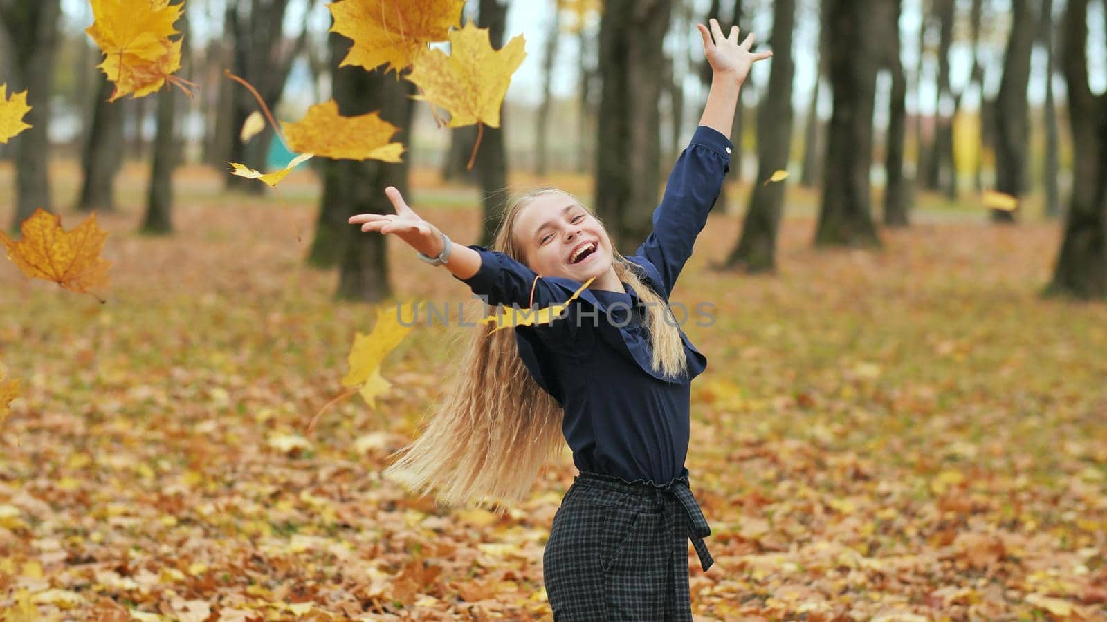 A young girl schoolgirl throws autumn leaves in a city park