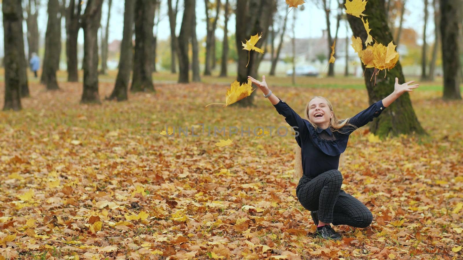 A young girl schoolgirl throws autumn leaves in a city park. Slow motion