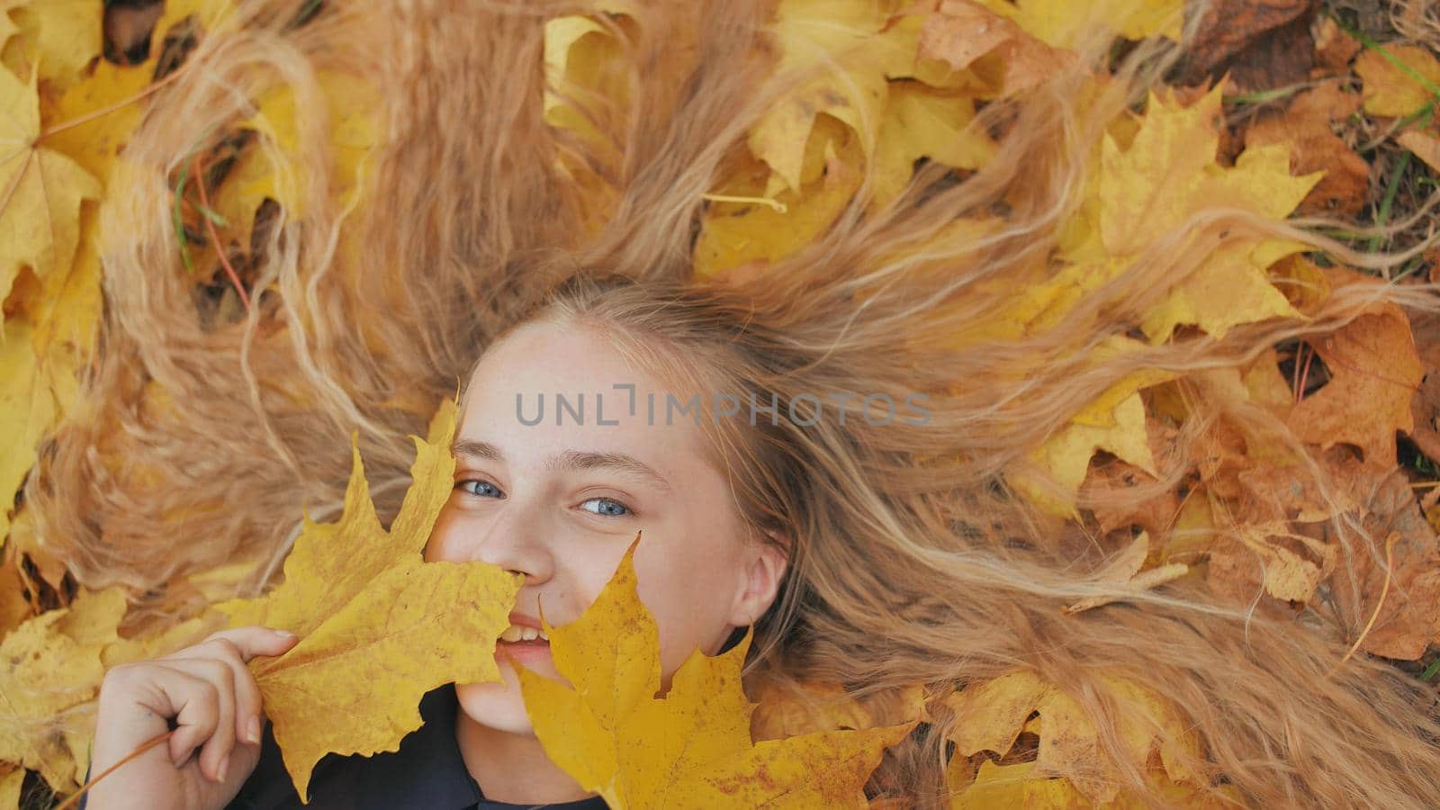 Young happy girl lies in autumn leaves and poses with maples leaves