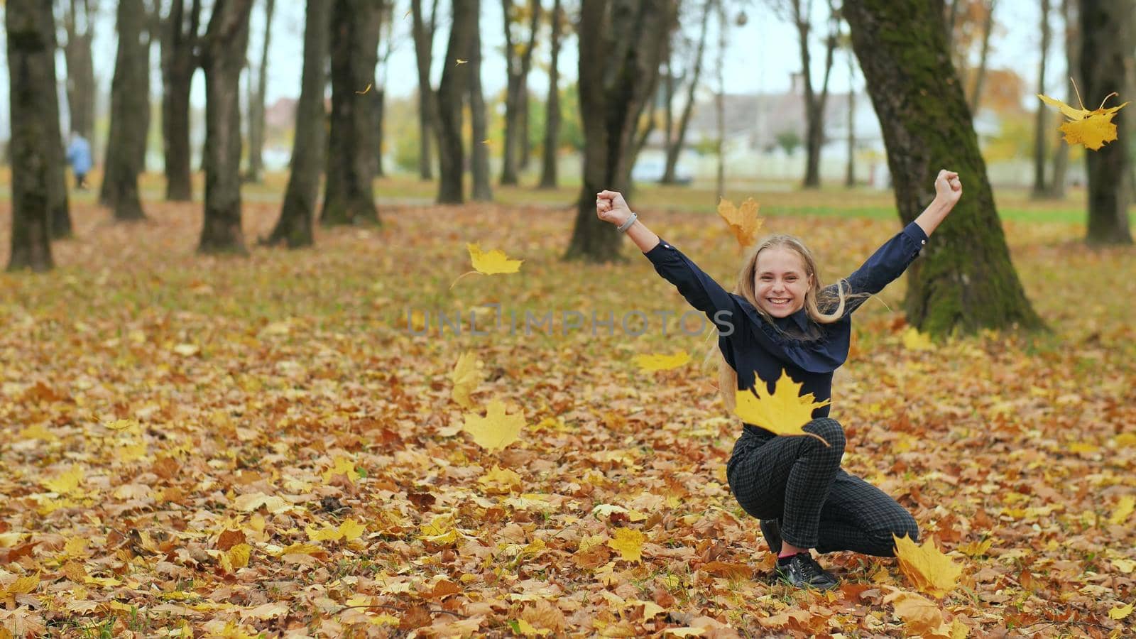 A young girl schoolgirl throws autumn leaves in a city park. Slow motion
