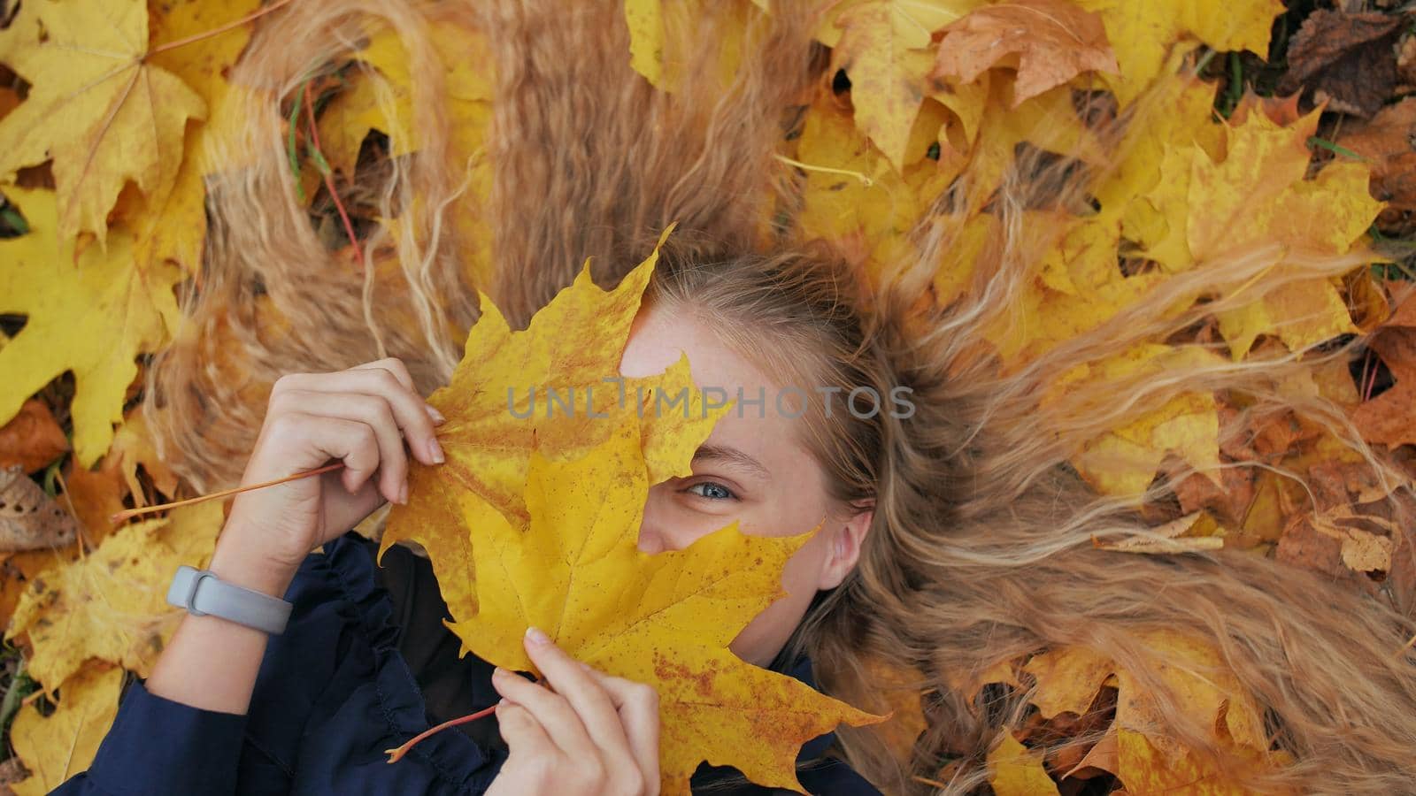 Young happy girl lies in autumn leaves and poses with maples leaves
