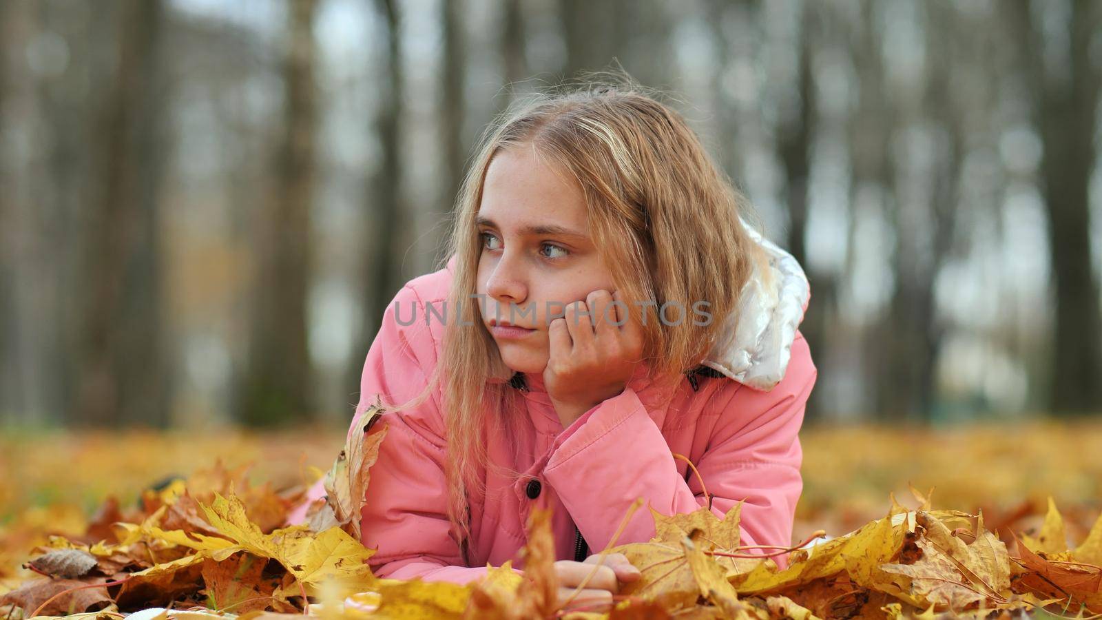 A little girl indifferently lies on the autumn foliage in a city park. She is very sad. by DovidPro