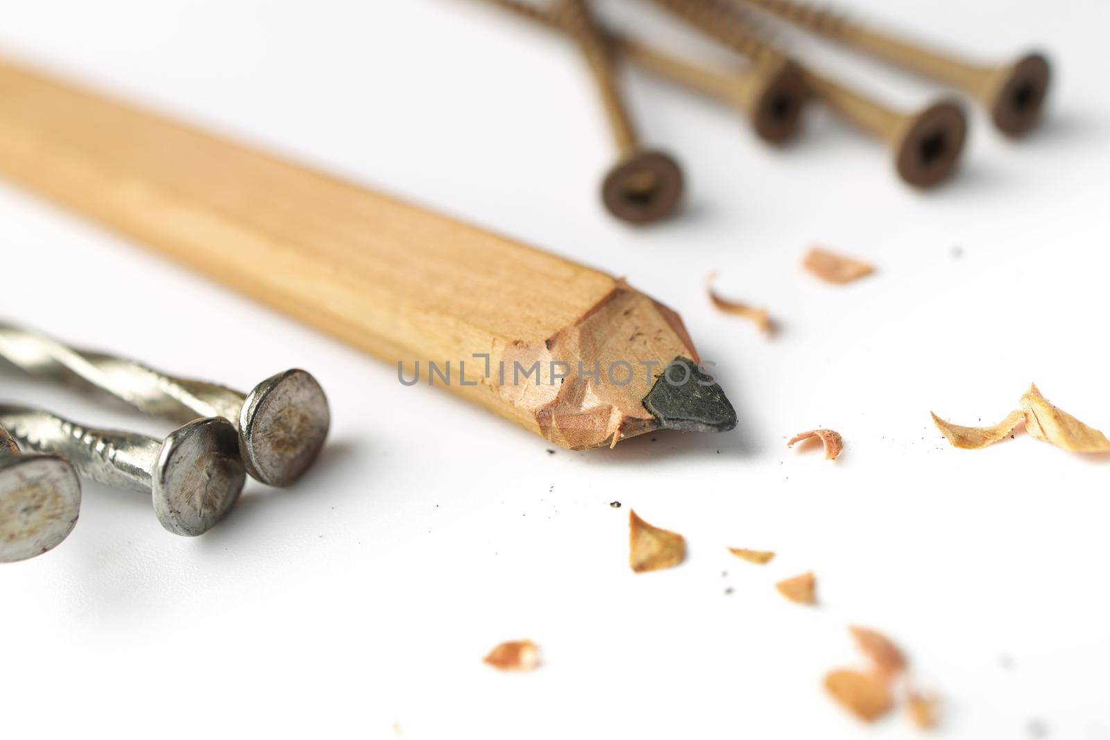 Low Angle Close up of a Carpenter's Pencil with Sharpening Shavings, Framing Nails and Deck Screws on a white background. High quality photo