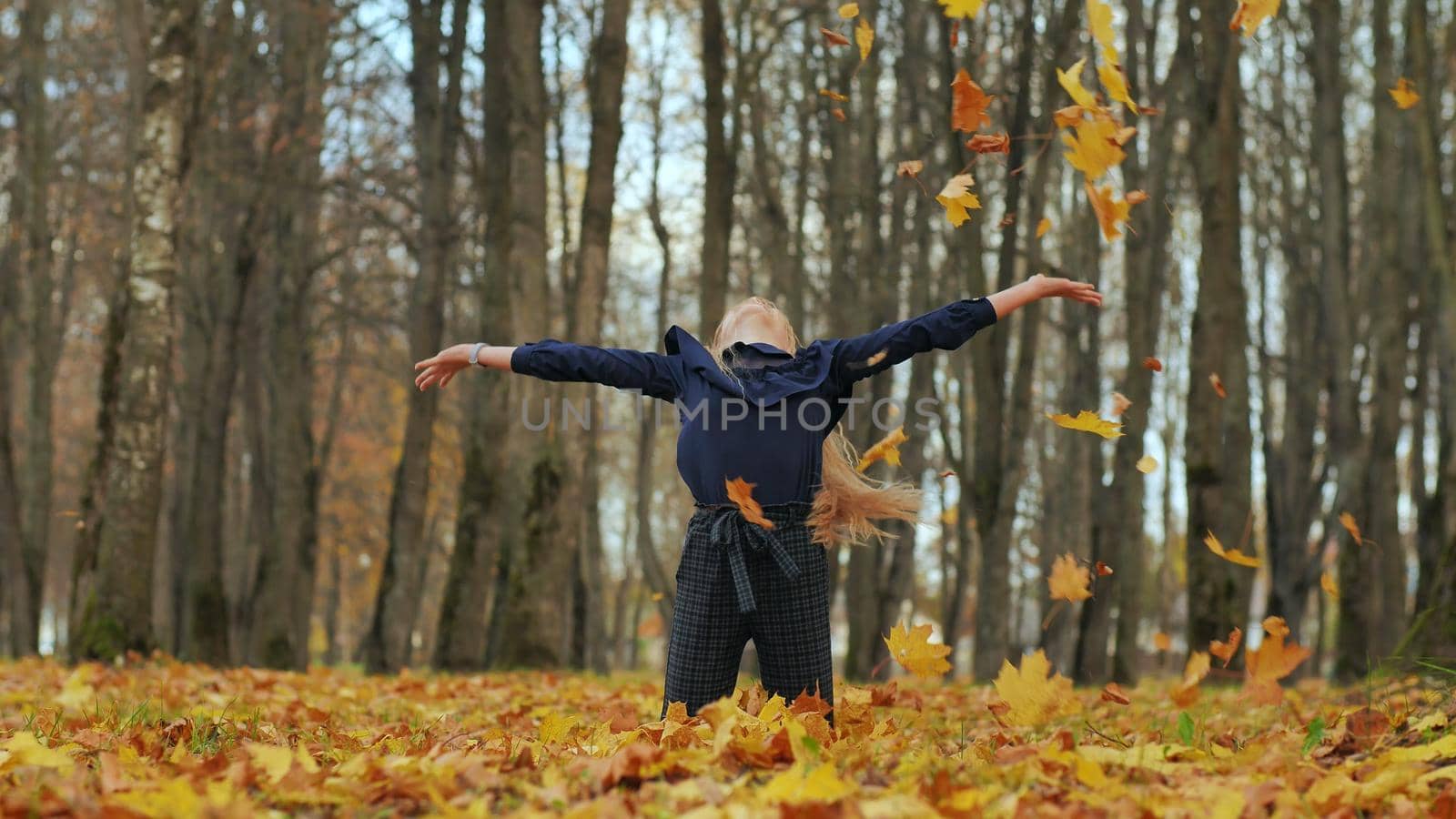 A young girl schoolgirl throws autumn leaves in a city park