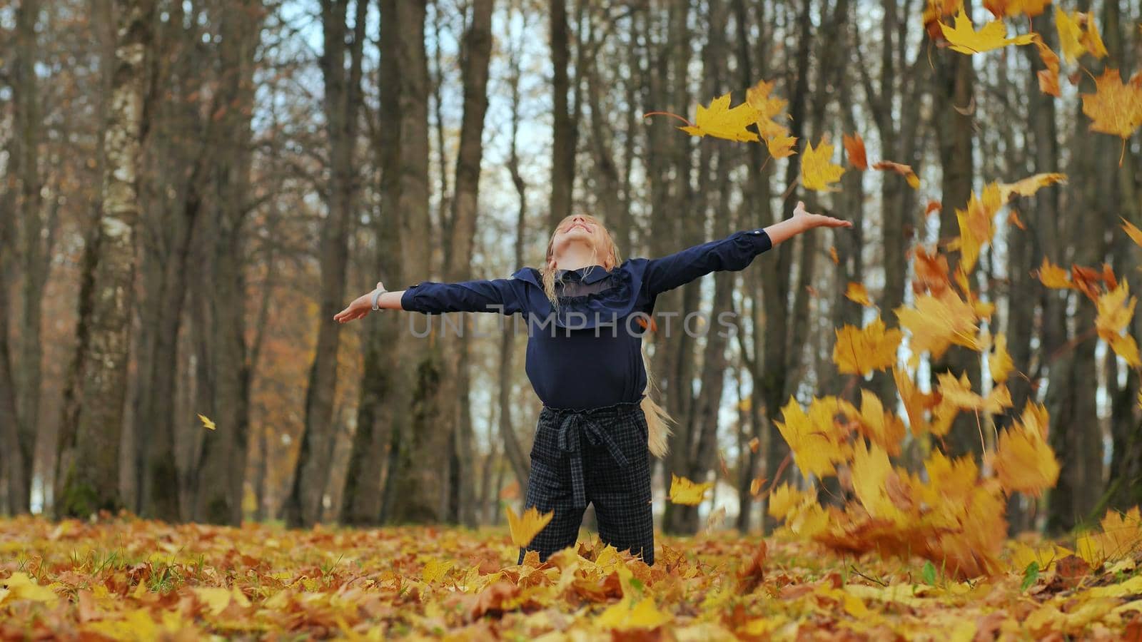 A young girl schoolgirl throws autumn leaves in a city park. by DovidPro