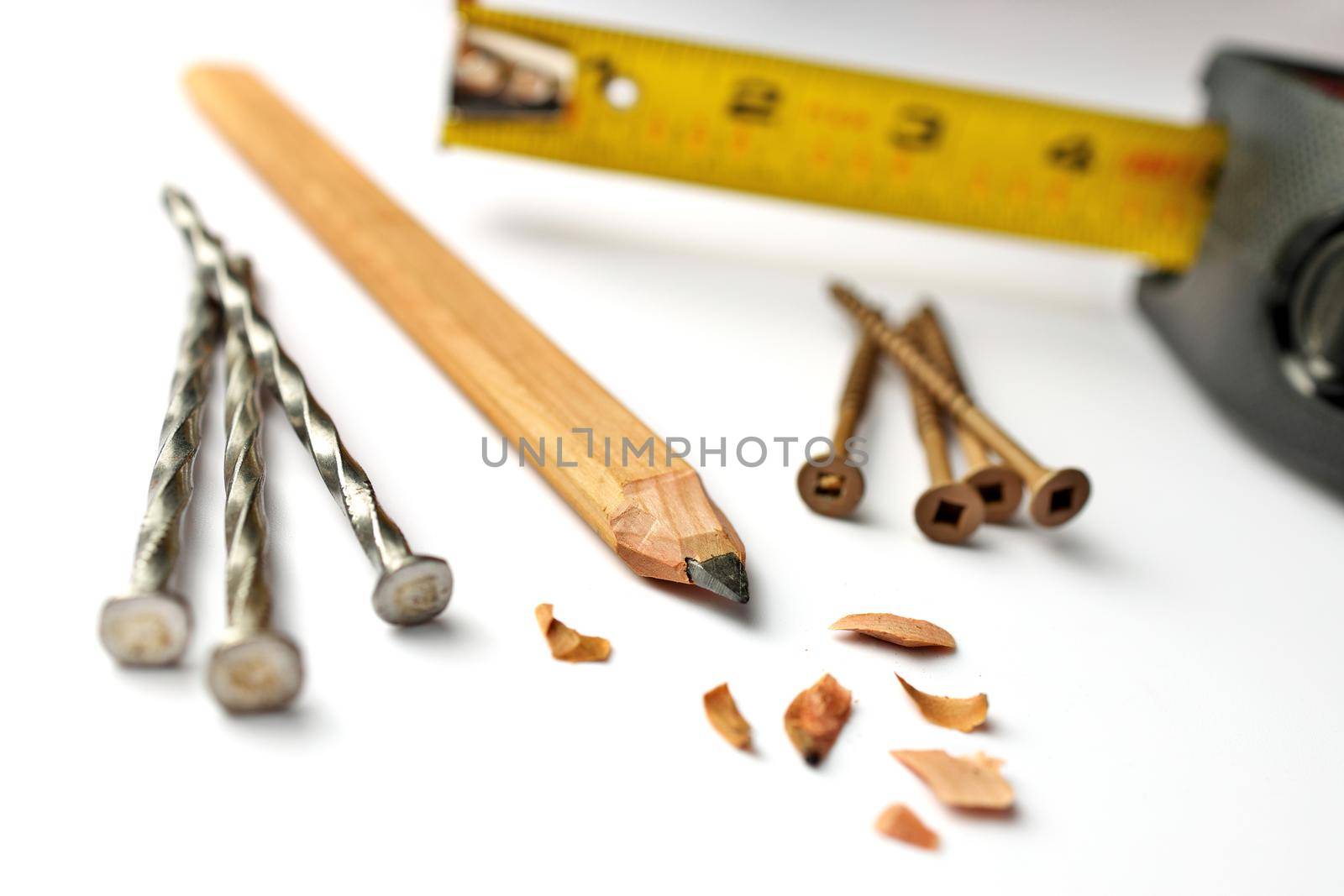 Low Angle Close up of a Carpenter's Pencil with Sharpening Shavings, Tape Measure, Framing Nails and Deck Screws on a white background. High quality photo