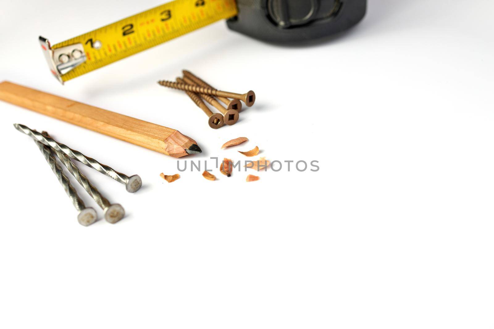 Low Angle Close up of a Carpenter's Pencil with Sharpening Shavings, Tape Measure, Framing Nails and Deck Screws on a white background. High quality photo