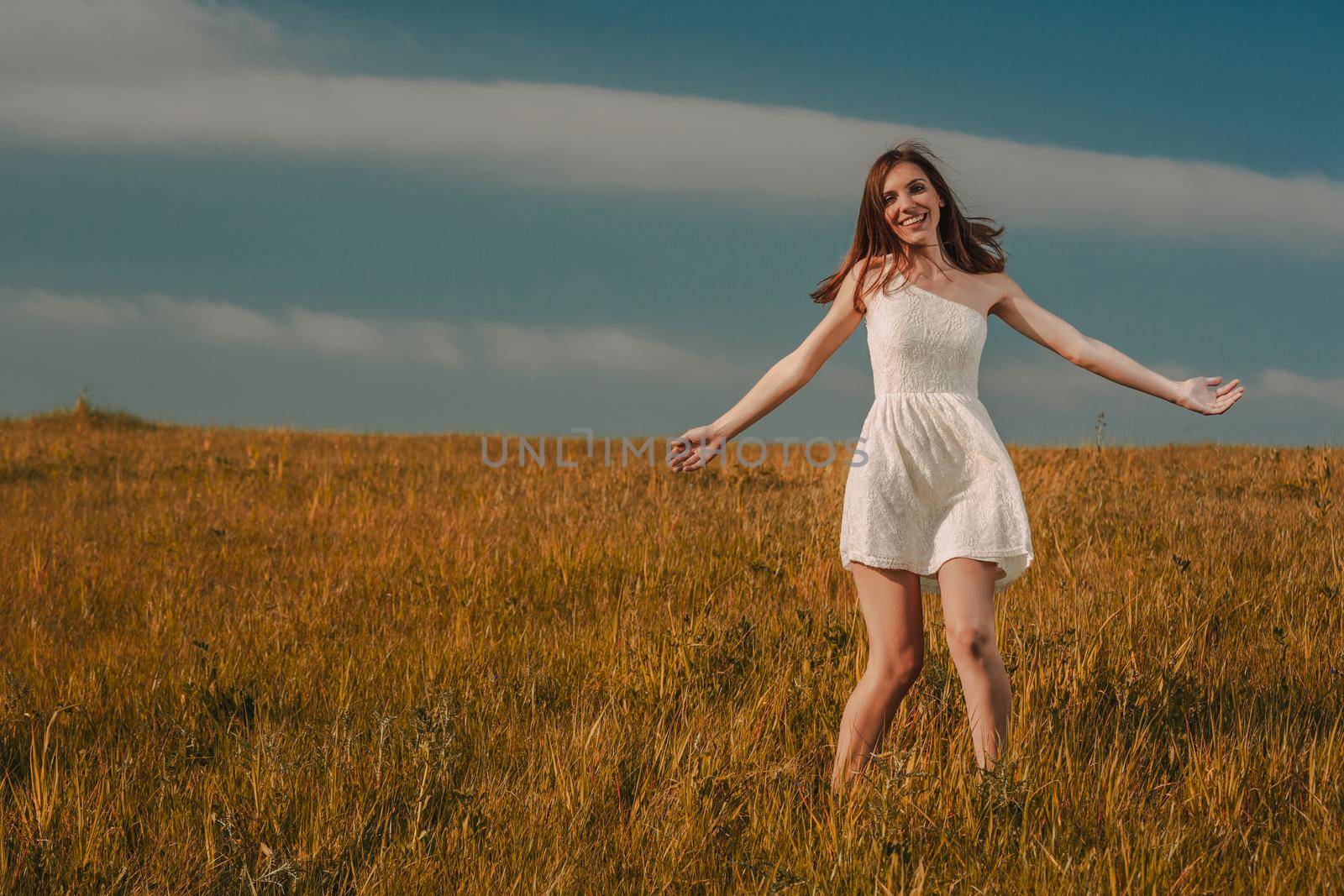 Young beautiful woman walking on a meadow wearing a white dress
