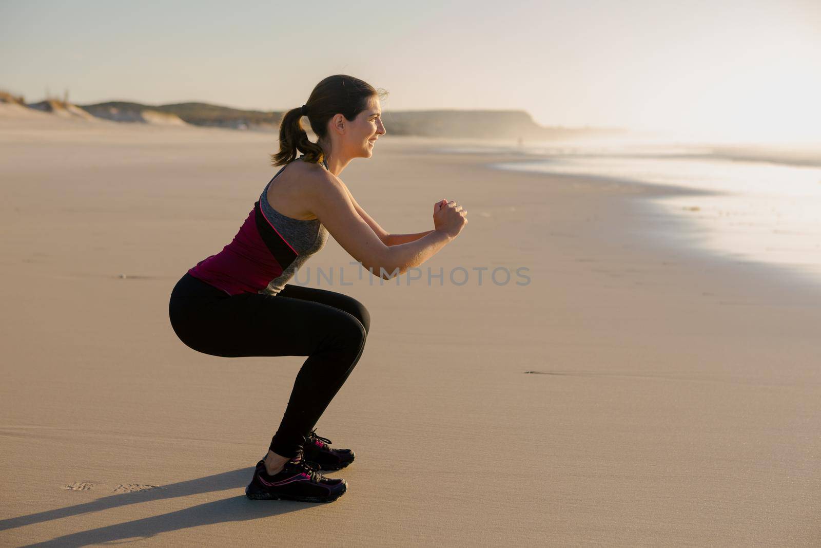 Shoot of a beautiful woman making squats exercises in the beach