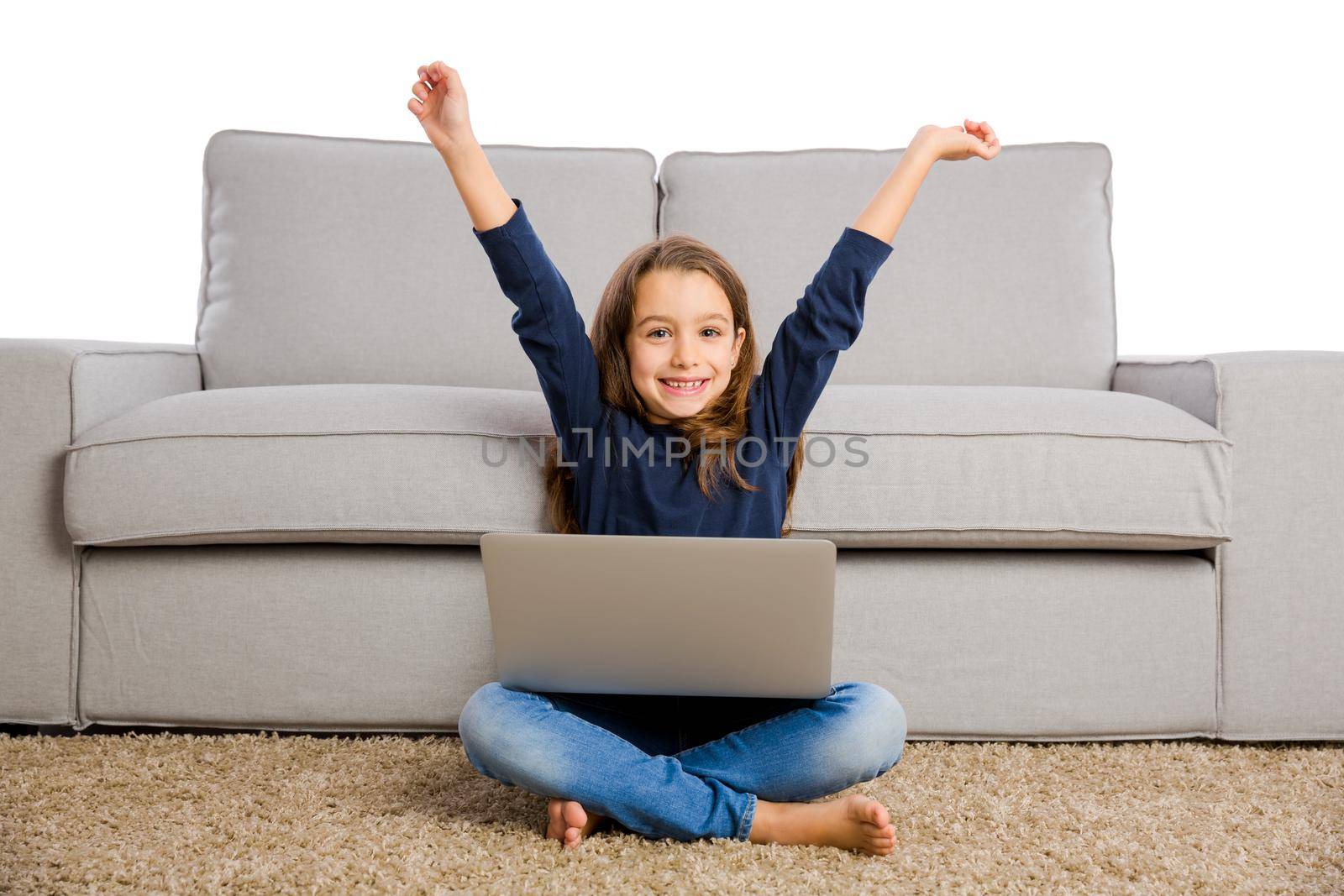 Happy little girl sitting on a couch with both arms up