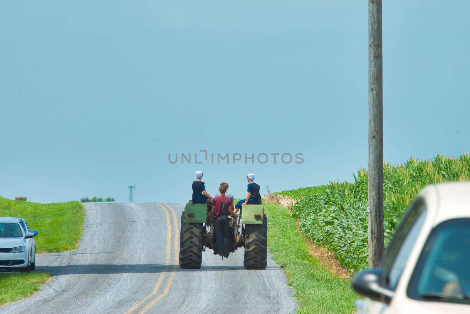 Amish Boy and Girl Teenagers Riding on a Old Tractor Thru Farmlands on a Summer Day