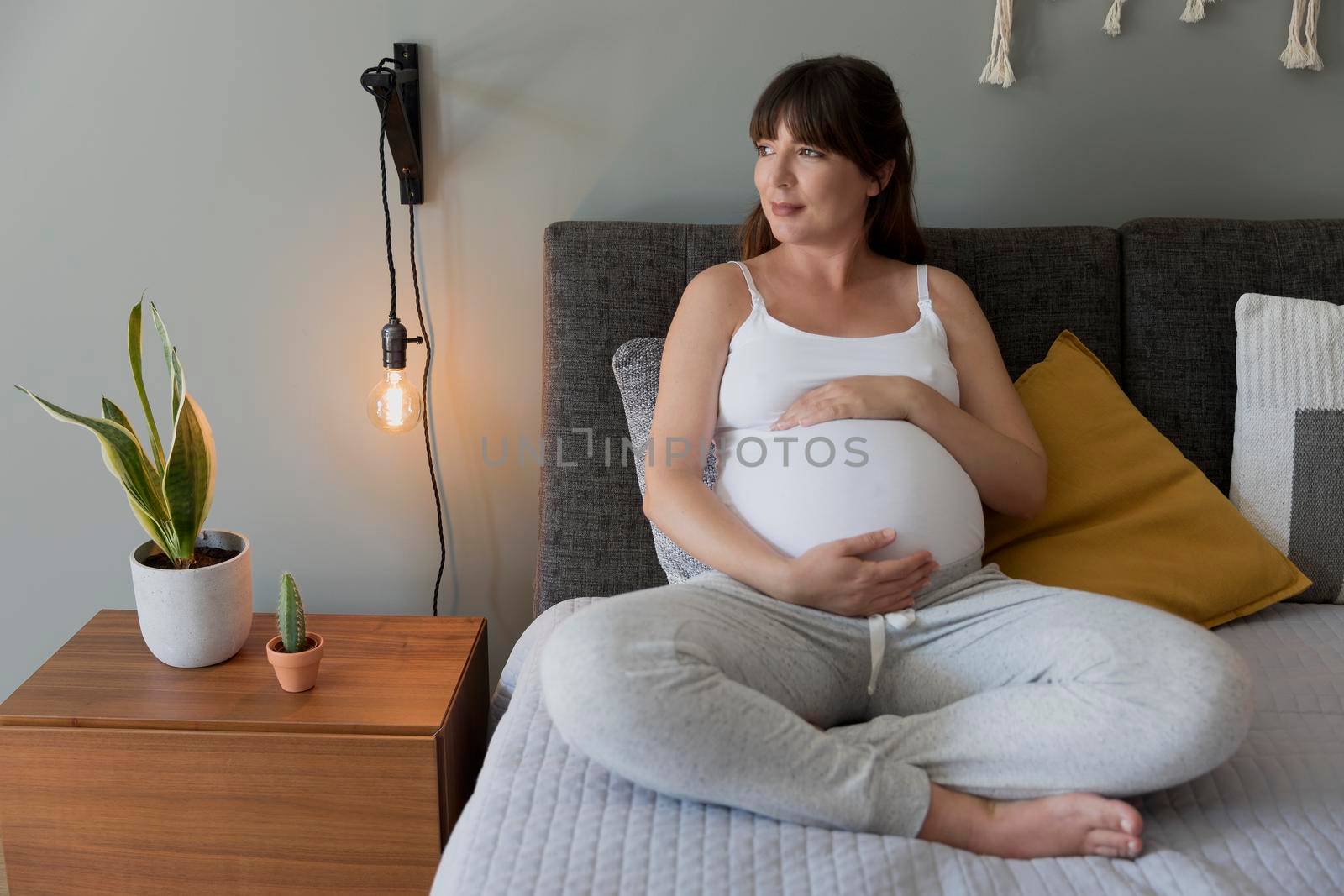 Happy pregnant woman sitting on bed and touching her belly at home