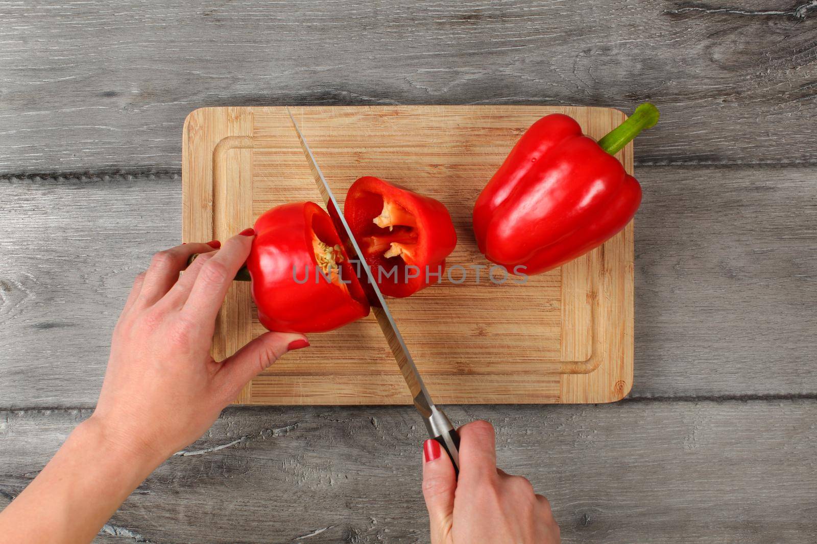 Table top view - woman hands holding chefs knife, cutting red bell pepper on chopping board.