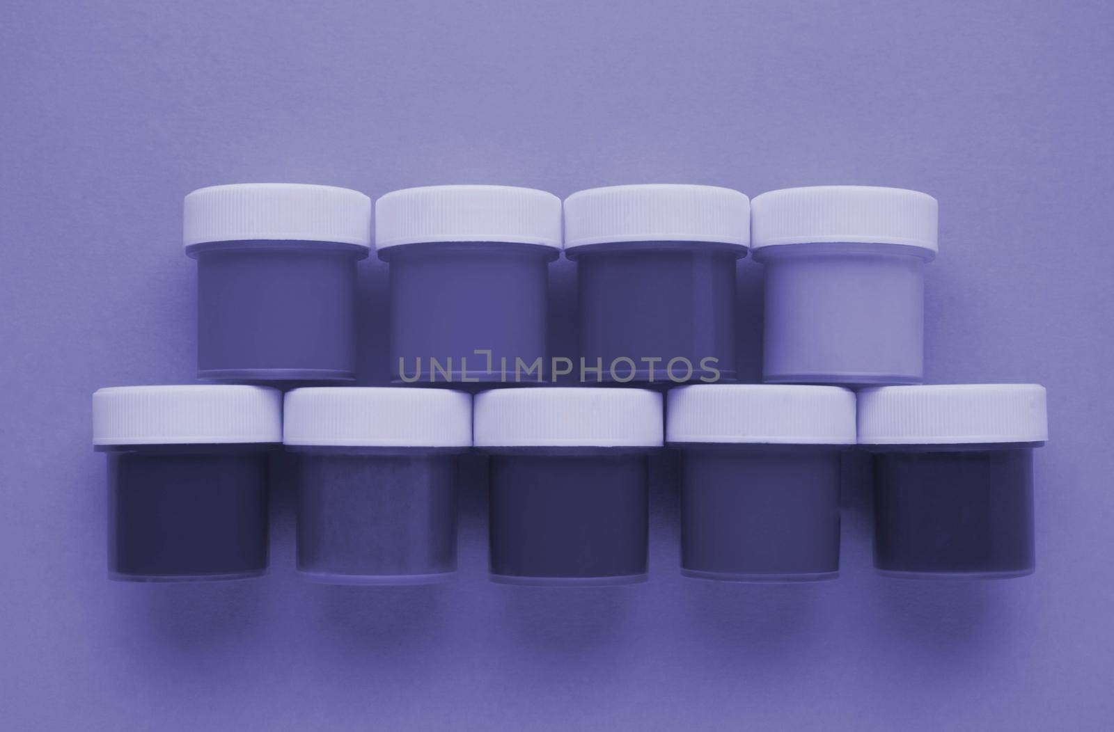 Closed plastic jars with gouache paint of different lilac shades for creativity on a lilac background. Materials for drawing, creativity, development. Very peri