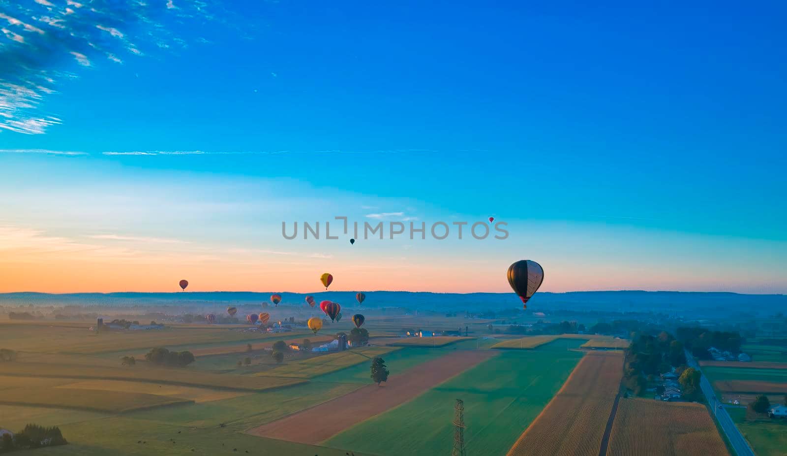 Aerial View of Many Hot Air Balloons In Flight Thru Rural Countryside On An Early Morning Balloon Festival