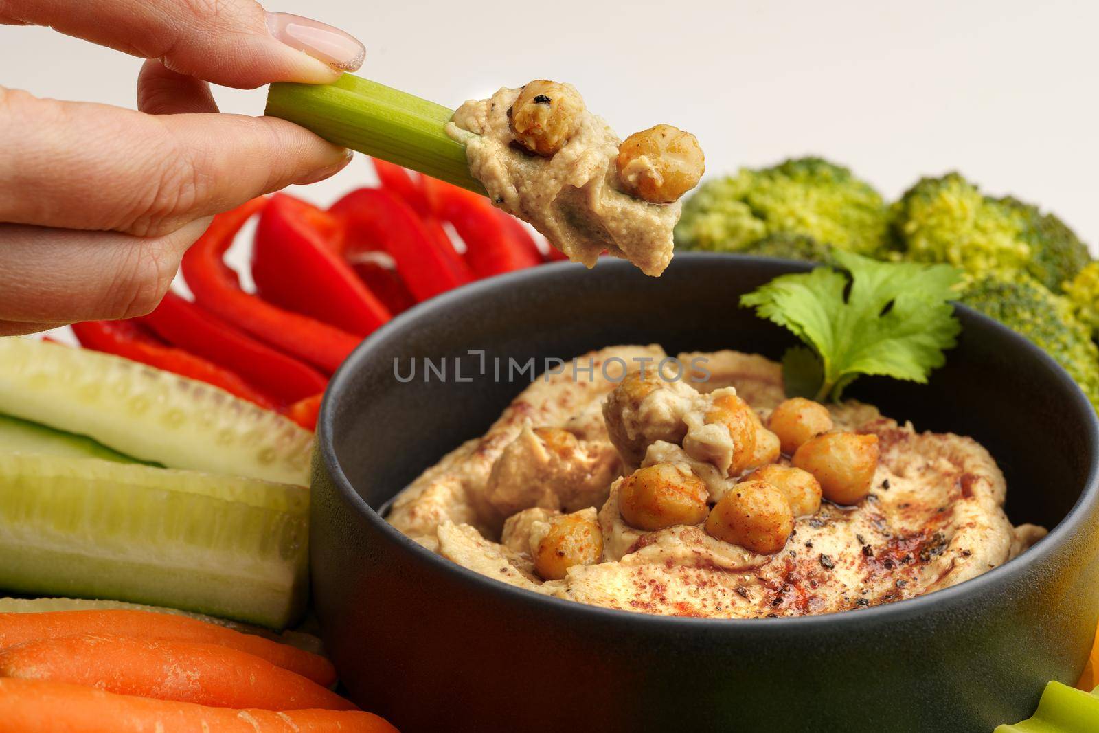 Closeup of woman hand holding celery stick with chickpeas hummus. Tasty hummus with vegetables and smoked paprika. High quality photo