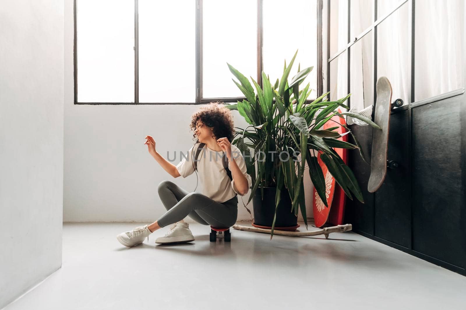 Carefree young mixed race woman dancing and listening to music with headphones sitting on skateboard. Copy space. Lifestyle concept.