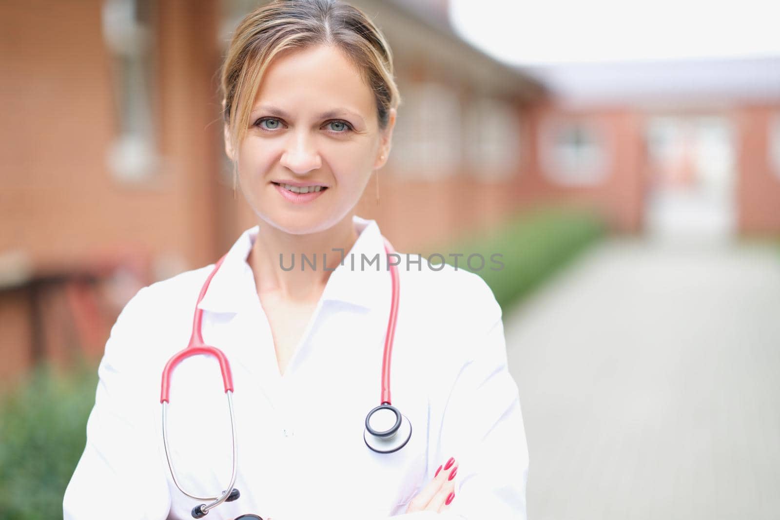 Doctor, a beautiful woman stands on the street against the background of the hospital, close-up, blurry. Ambulance service, clinic staff