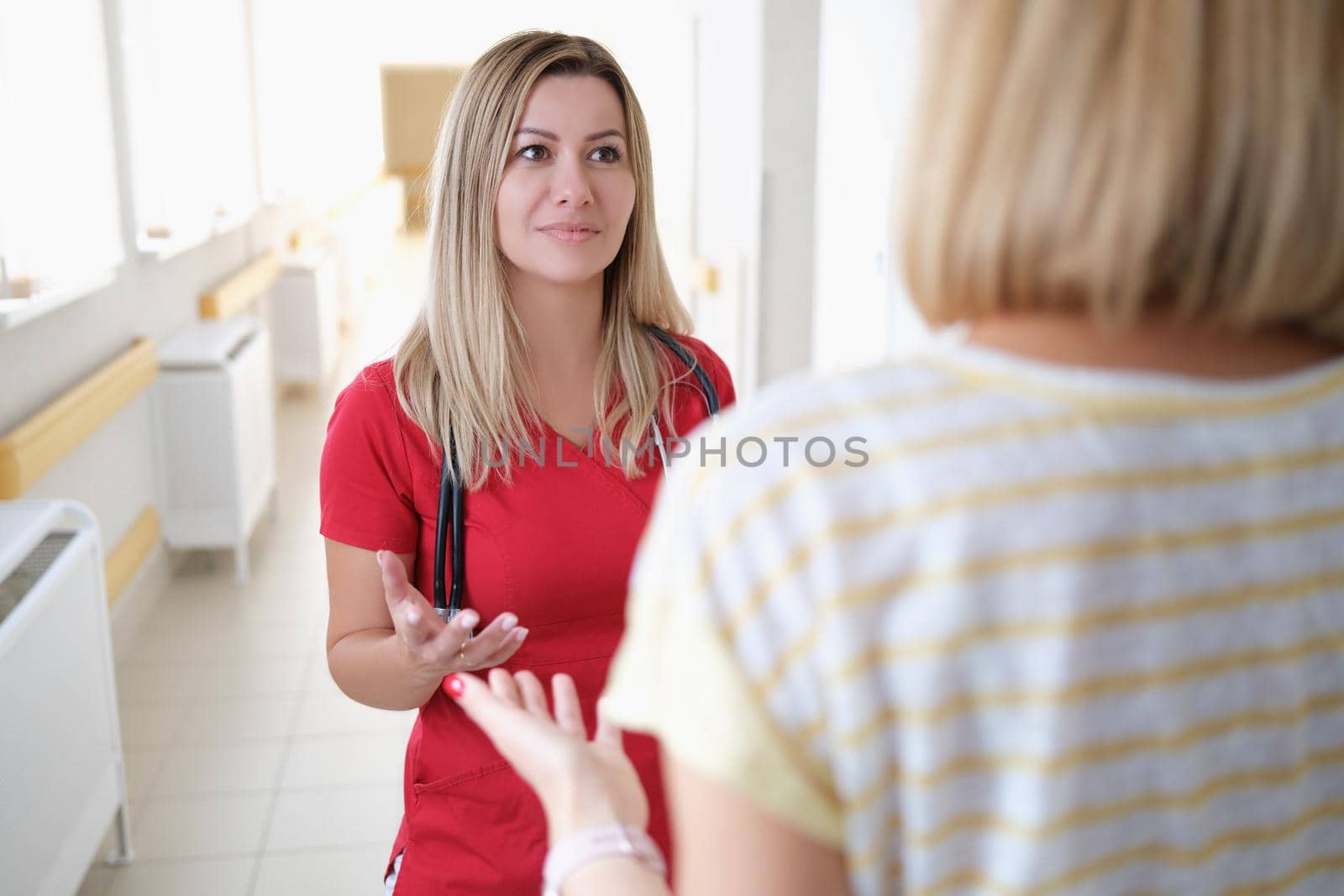 A doctor in listens to a woman in the hospital corridor by kuprevich