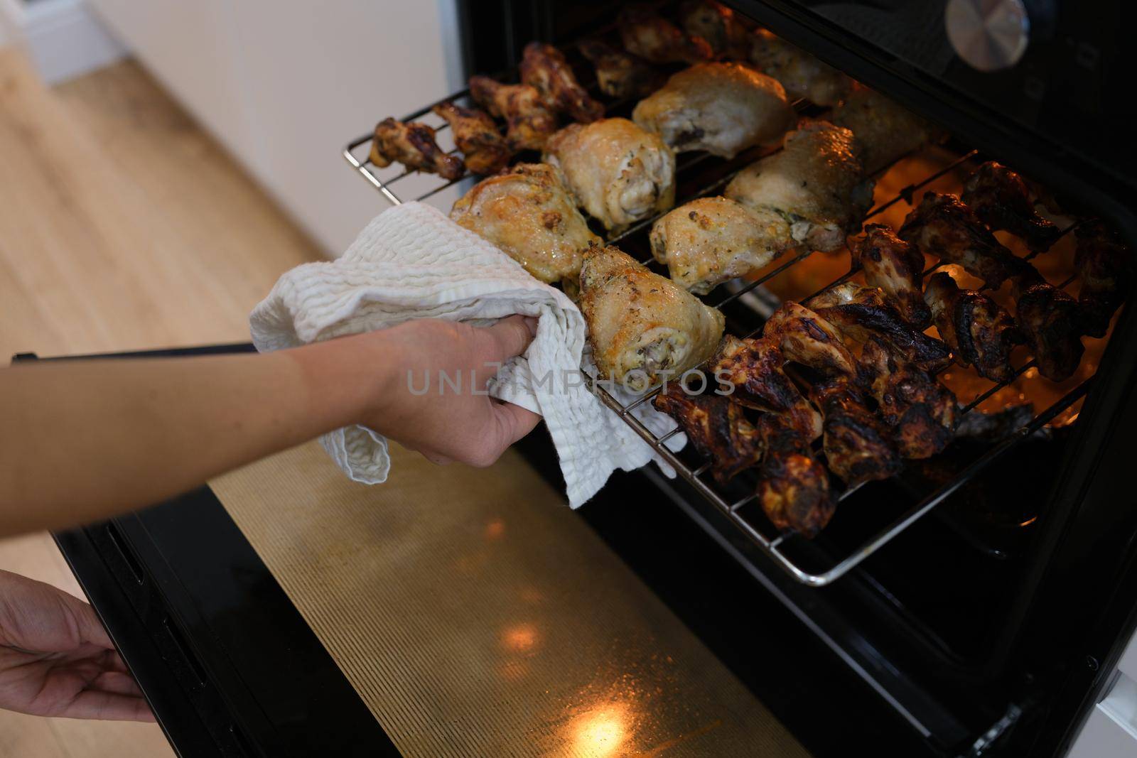 A woman takes out ready-made chicken wings and legs from the oven, close-up. Crispy chicken meat, home cooking