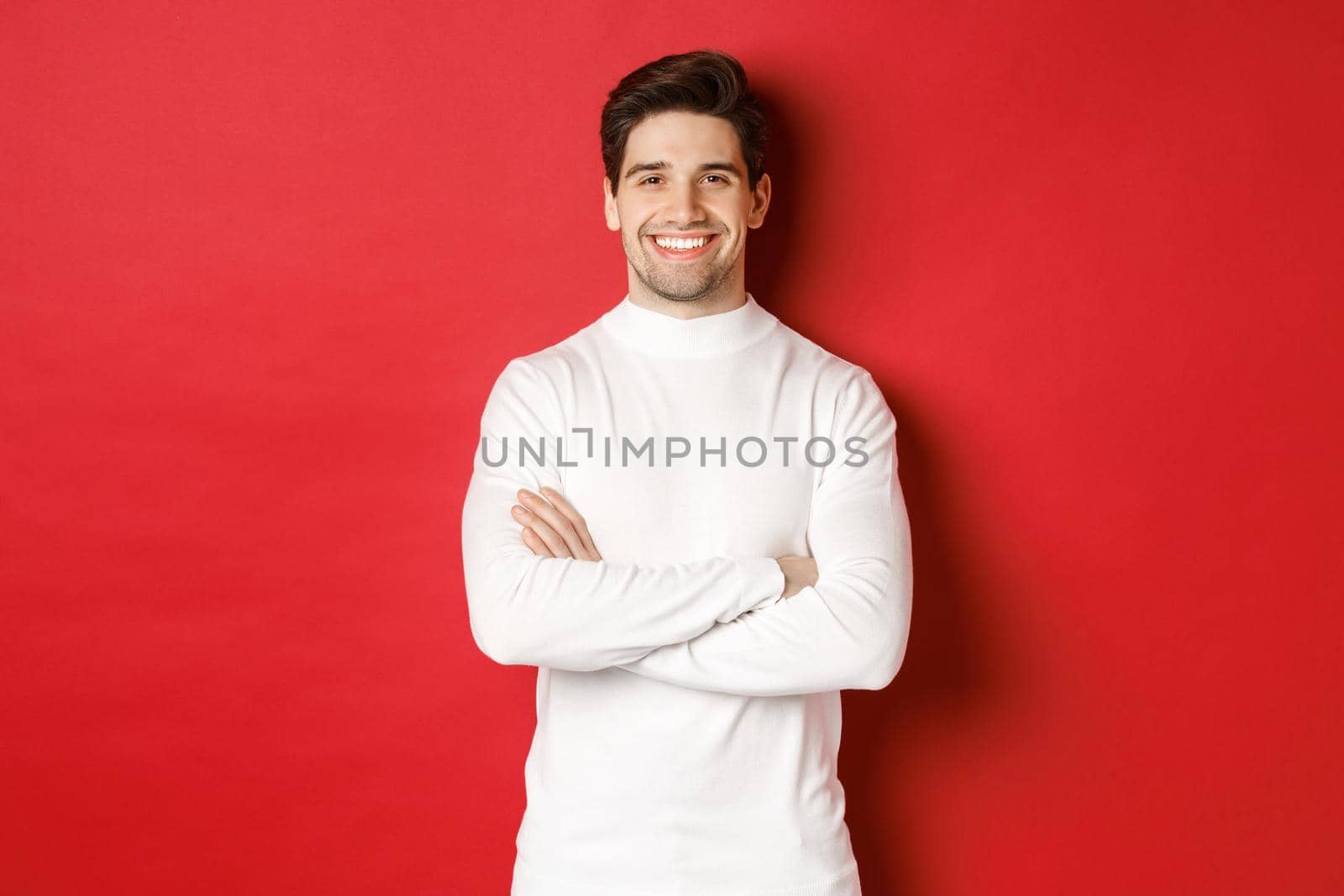 Concept of winter holidays, christmas and lifestyle. Portrait of confident good-looking man with bristle, wearing white sweater, cross arms on chest and smiling satisfied by Benzoix