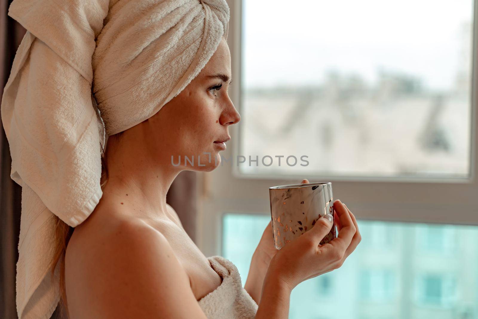 Young serene relaxed woman in spa bath towel drinking hot beverage tea coffee after taking shower bath at home. Beauty treatment, hydration concept by Matiunina