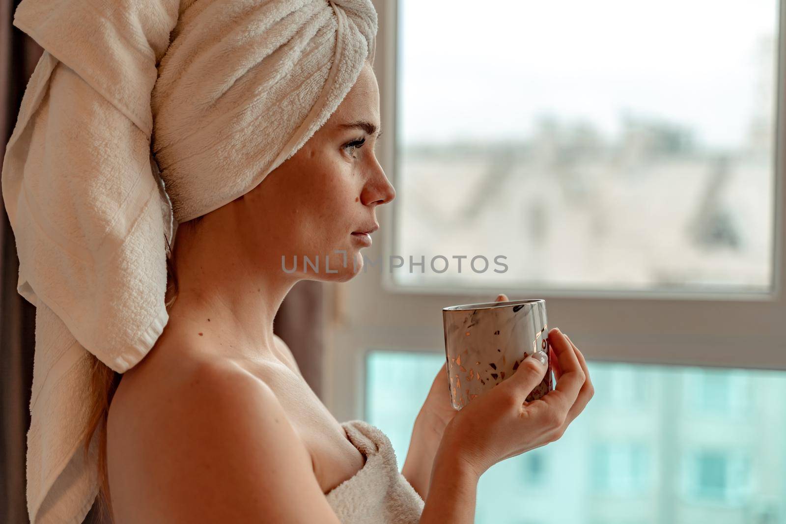 Young serene relaxed woman in spa bath towel drinking hot beverage tea coffee after taking shower bath at home. Beauty treatment, hydration concept.