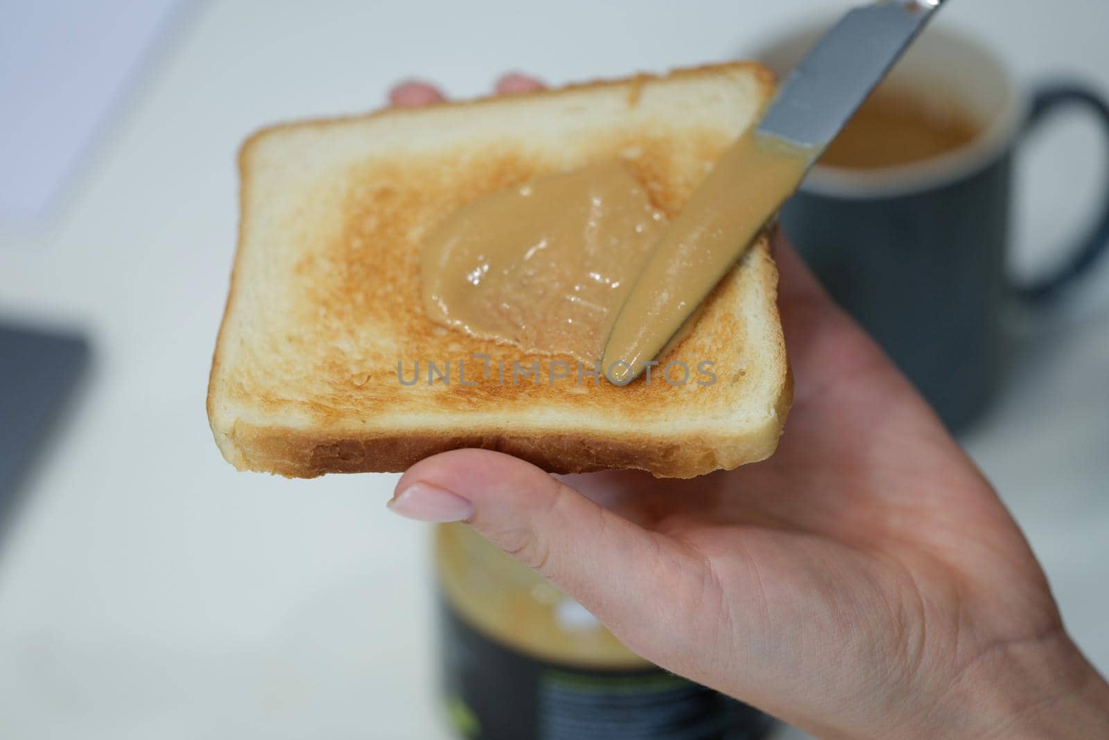 A hand smears peanut butter on a crispy toast made from bread. Traditional homemade American breakfast, unhealthy snack