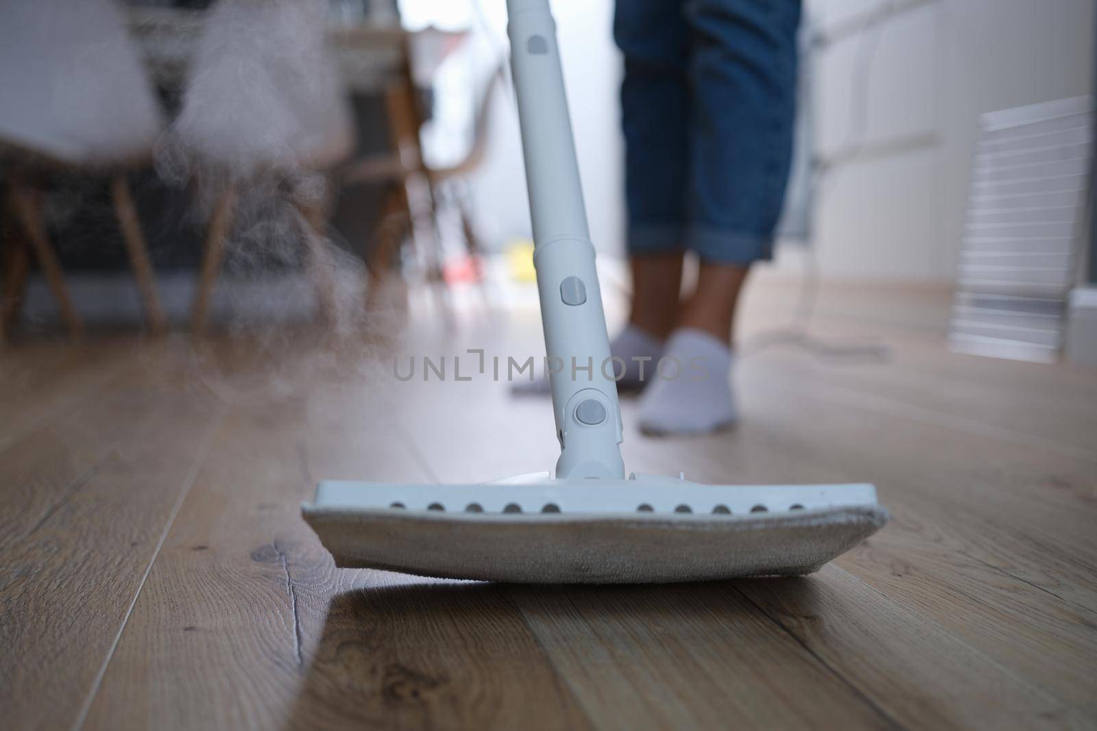 A steam mop washes the wooden parquet on the floor, close-up, blurry. Apartment cleaning, laminate flooring