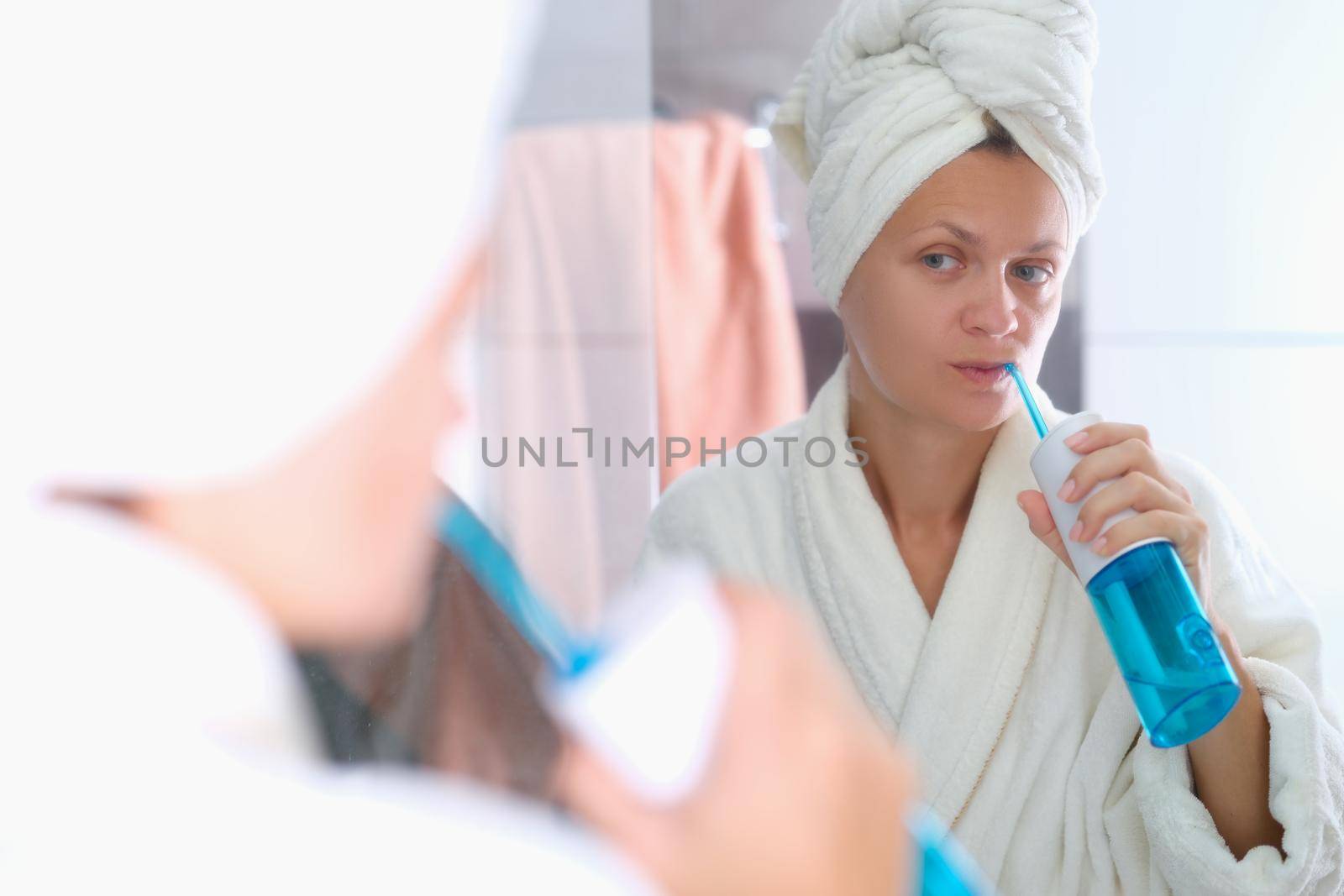 A woman in a dressing gown with a towel on her head is brushing her teeth with an irrigator. Oral hygiene, beauty and health