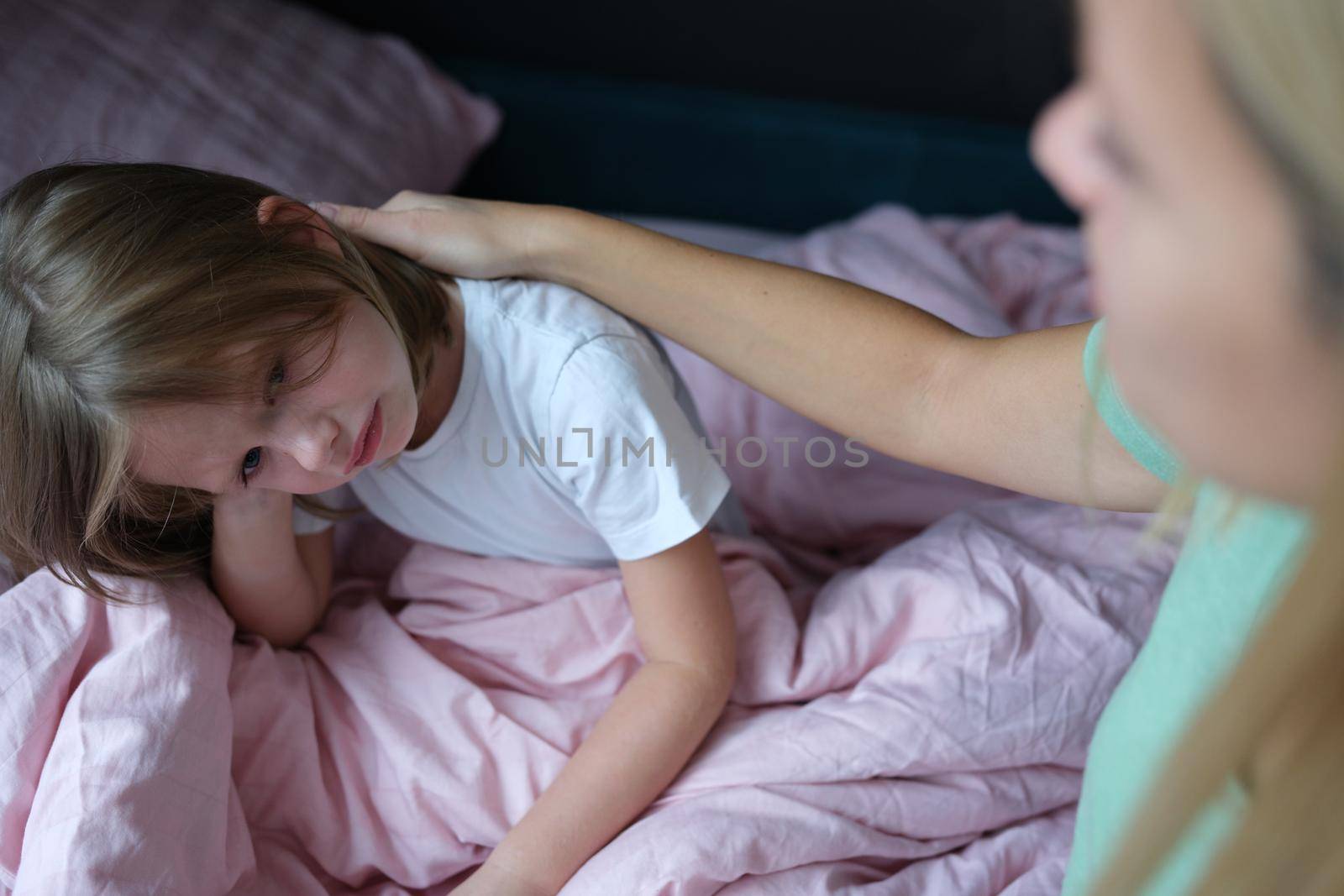 Mom stroking a frustrated little girl on the bed, close-up, blurry. Sad child, insomnia, bad dream, anxiety