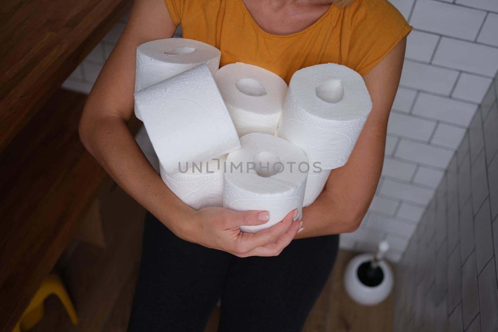 Woman in the toilet holds many rolls of toilet paper, close-up. Empty shelves, stock of personal care products