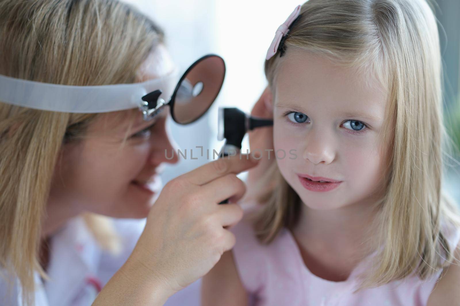 Cute little girl lets the doctor check the woman's ear, close-up, blurry. Pediatrician smiling while examining a child