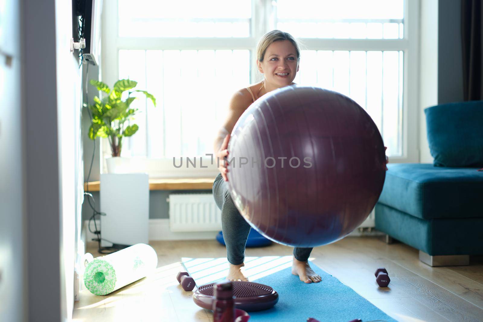 Woman doing squats with a burgundy ball at home by kuprevich