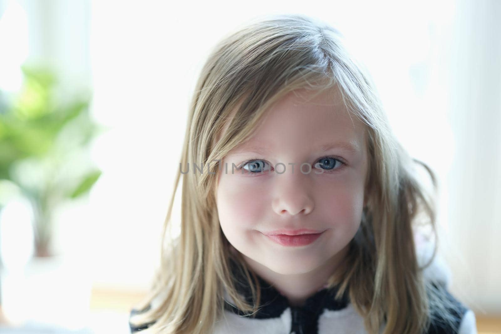 Portrait of a cute blonde girl close-up. Happy child smiles, positive emotions, naive look. The kind face of a little european girl