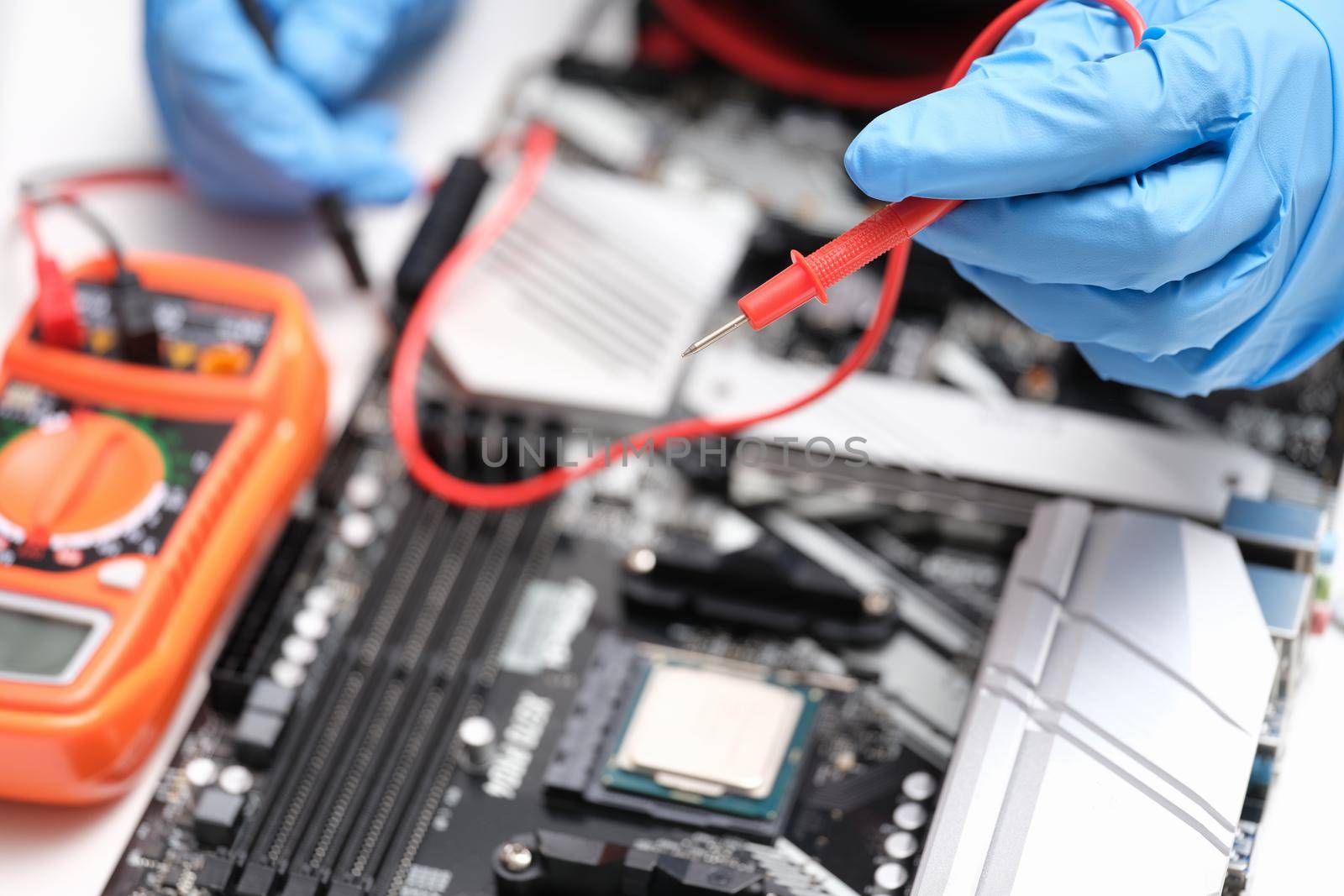 Hands in blue gloves to check electronic equipment with a multimeter, close-up. Repair, electrical troubleshooting, short circuit