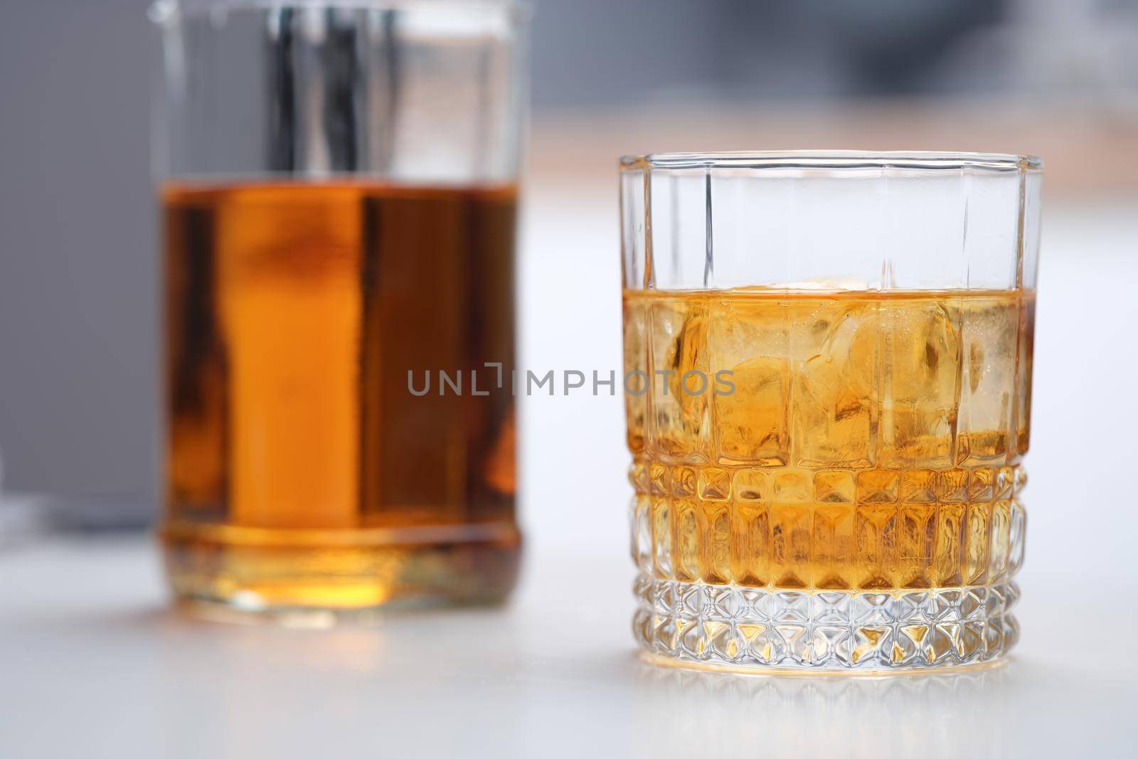 Brown alcoholic cocktail with ice in a wide glass, close-up. Incomplete whiskey bottle and glass on gray table background