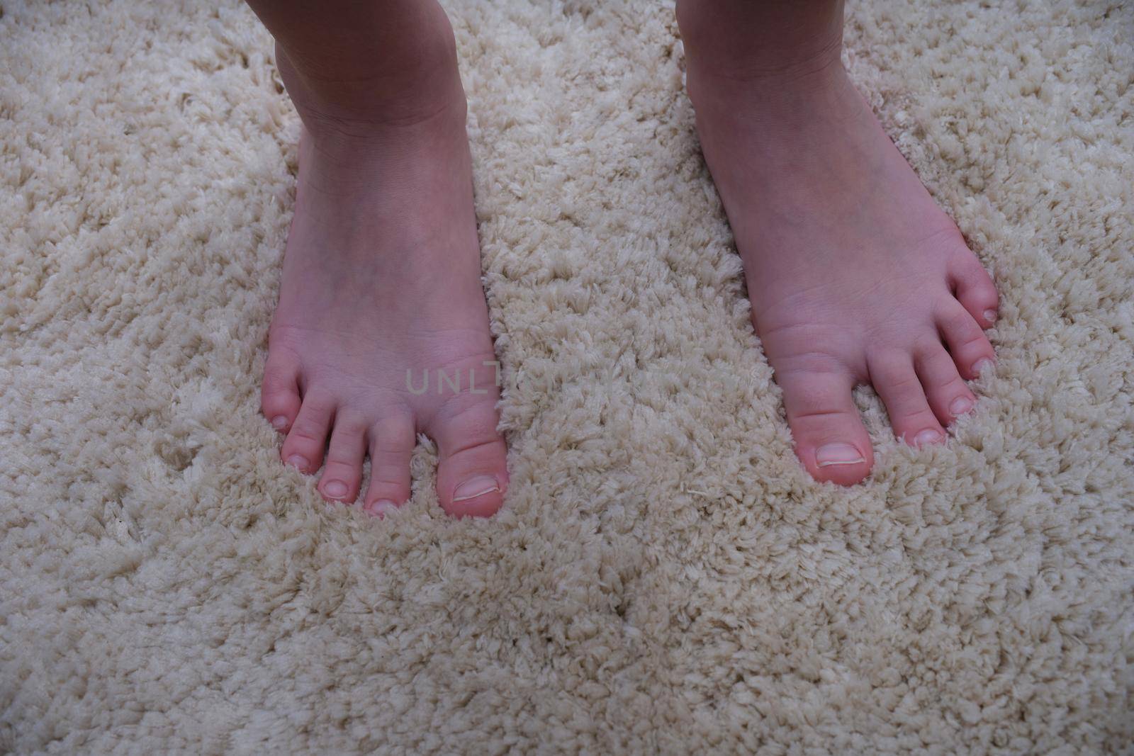 Close-up of an adult's bare feet on a soft carpet. Warm floor in the apartment. Foot massage. Toes without pedicure