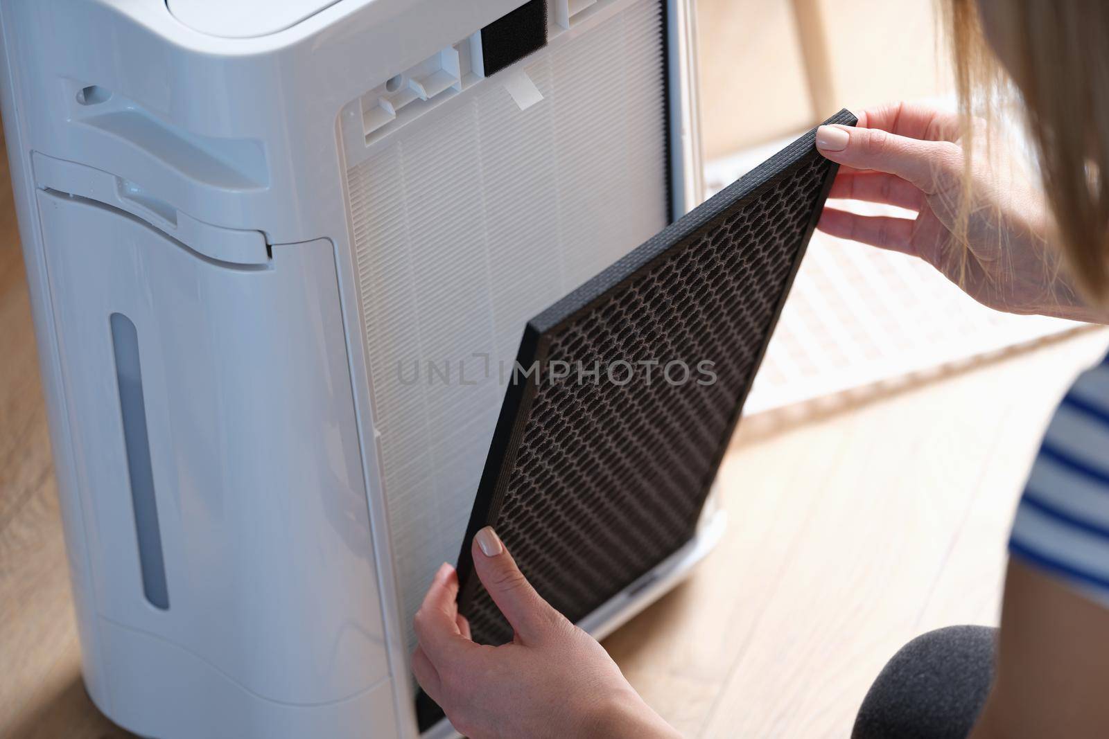 A woman removes a replaceable filter of an air purifier by kuprevich