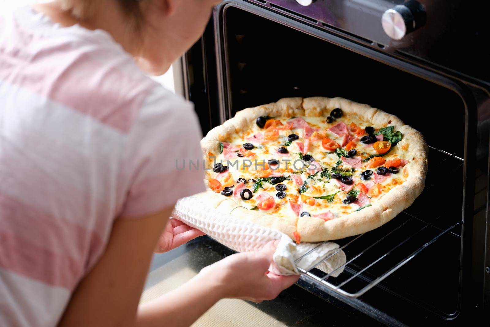 A woman takes out a round homemade pizza from the oven, close-up. Home kitchen appliances for cooking