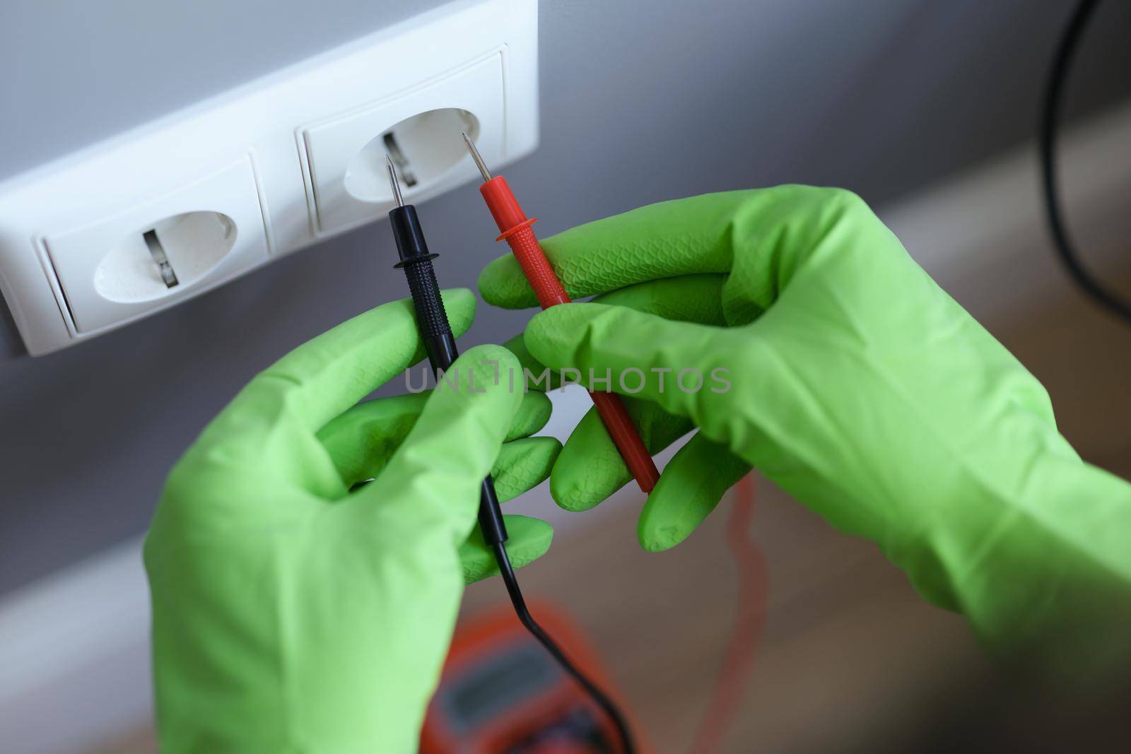 Hands in green gloves plug the voltmeter into an outlet, close-up. Home electrical wiring repair, electrician equipment